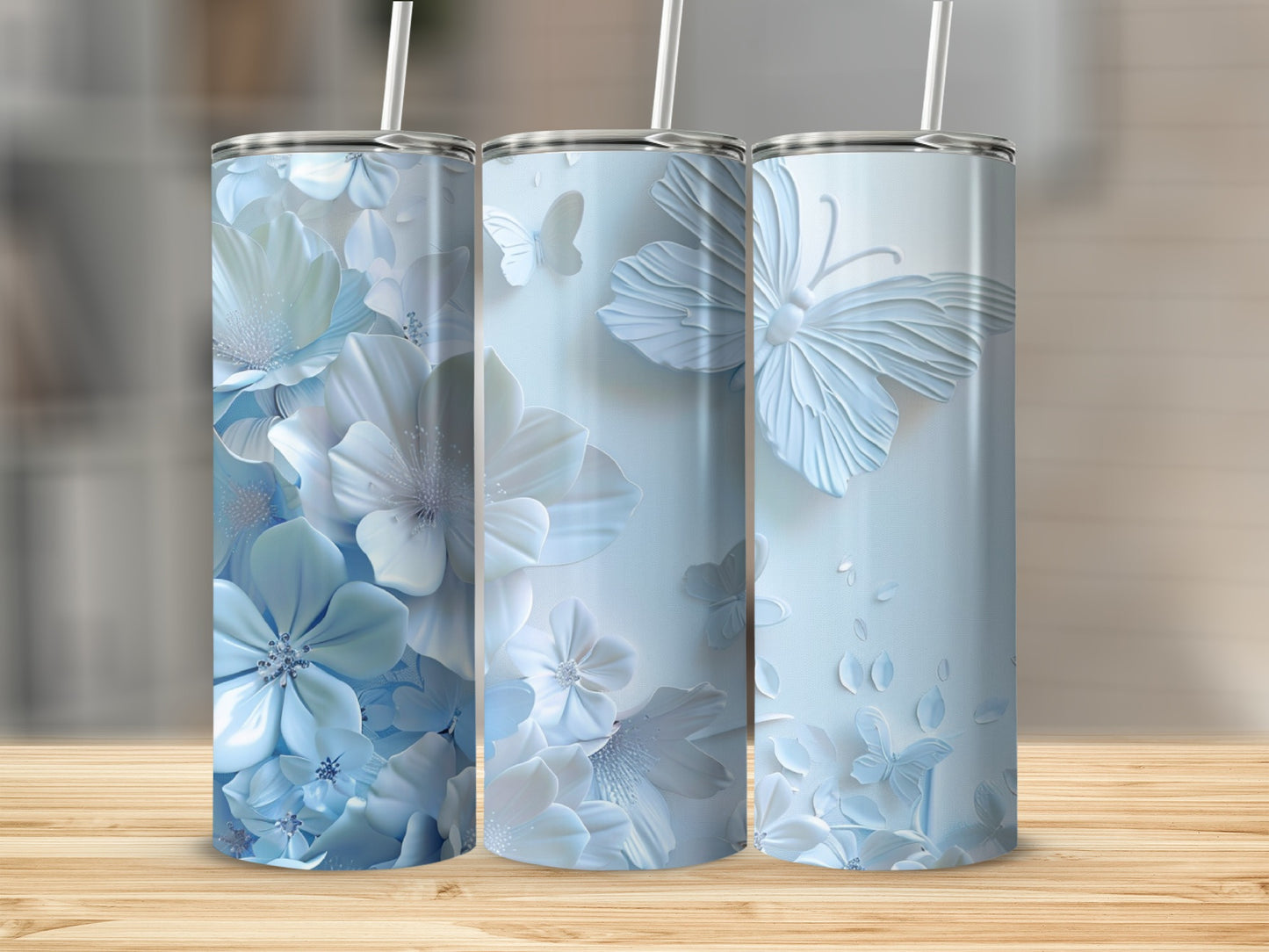 Three blue floral and butterfly tumblers with straws on a wooden surface.