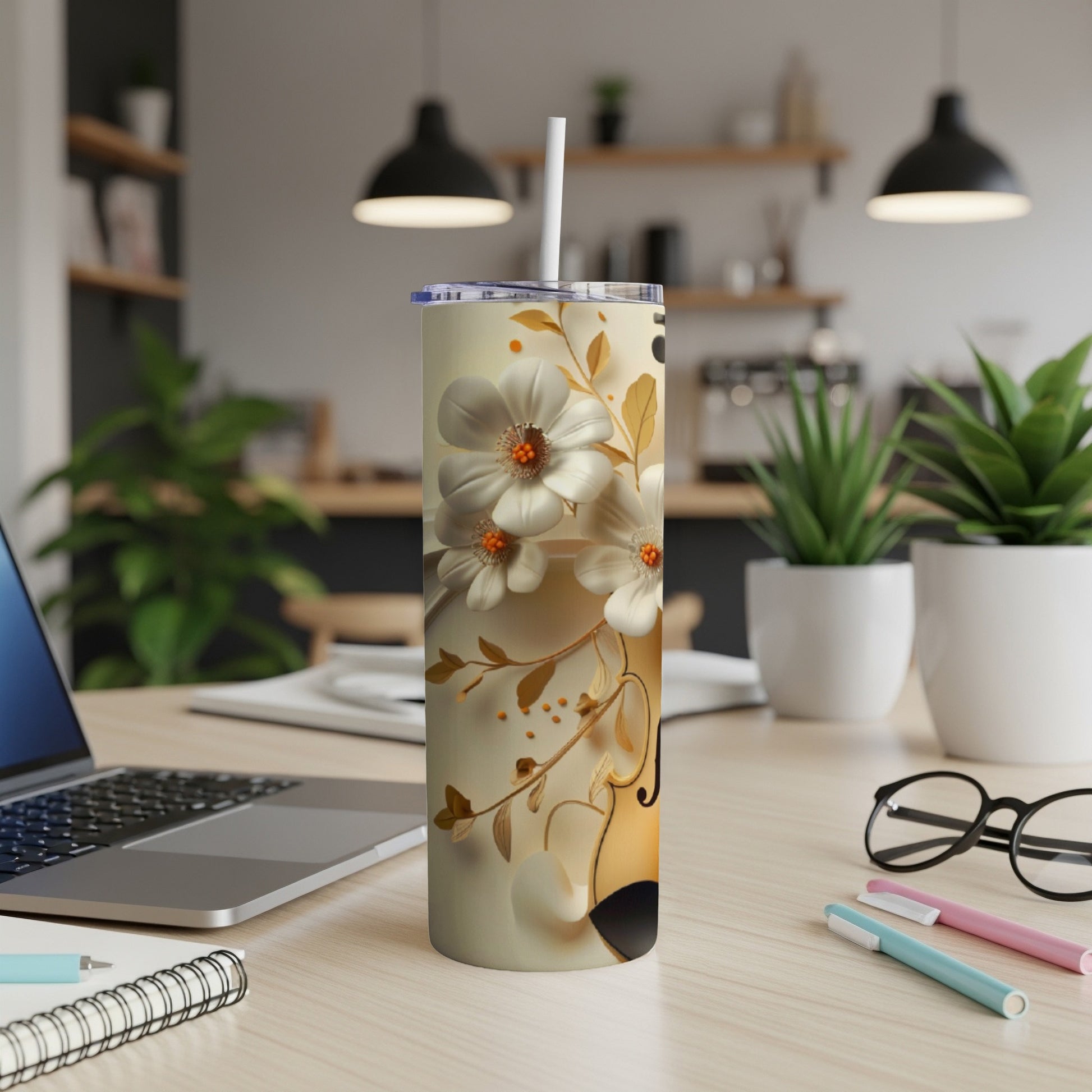 Floral and violin design on a white tumbler with a straw, on a desk.