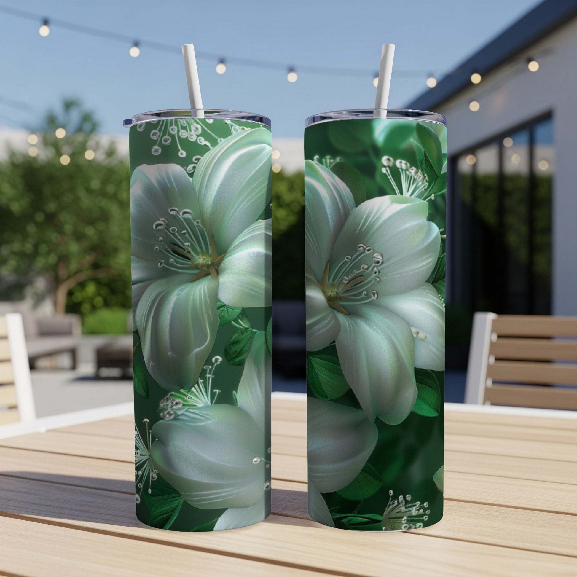 Two white floral tumblers with straws on a wooden table outdoors.
