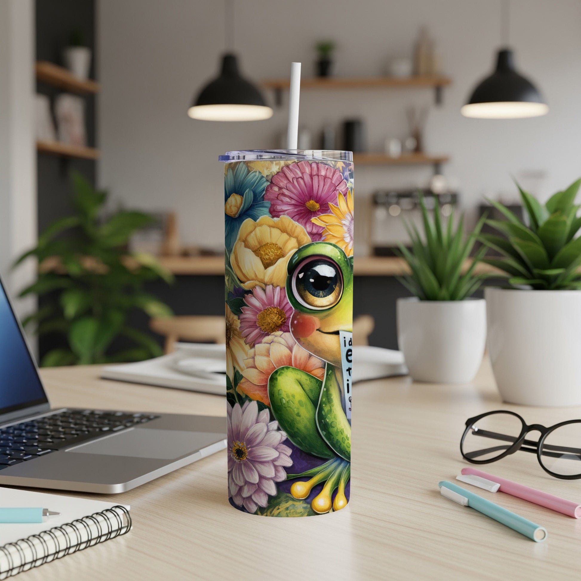 Cute frog with flowers on a tumbler with a straw, resting on a desk.