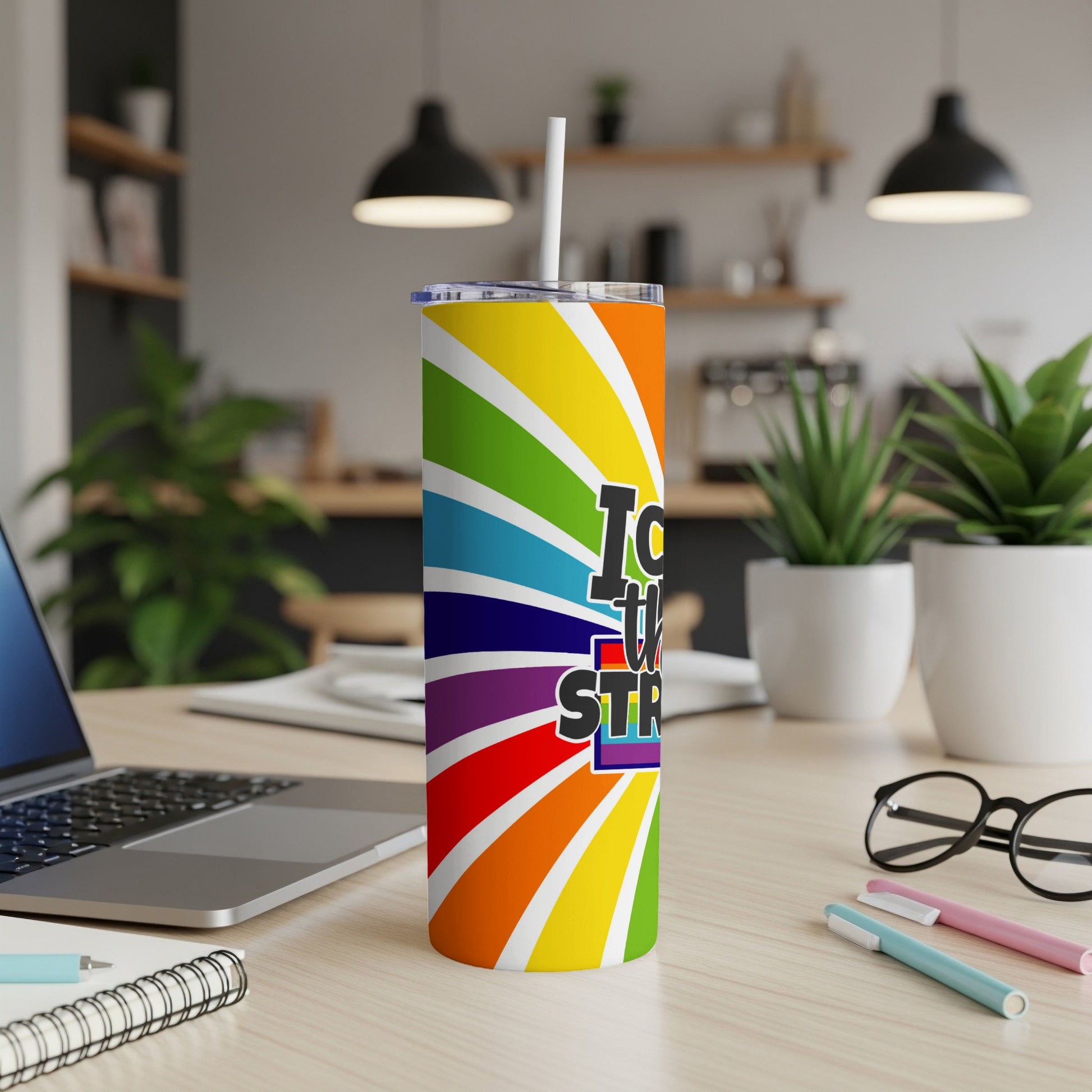Rainbow striped tumbler with "Love is STR..." text, on a desk.