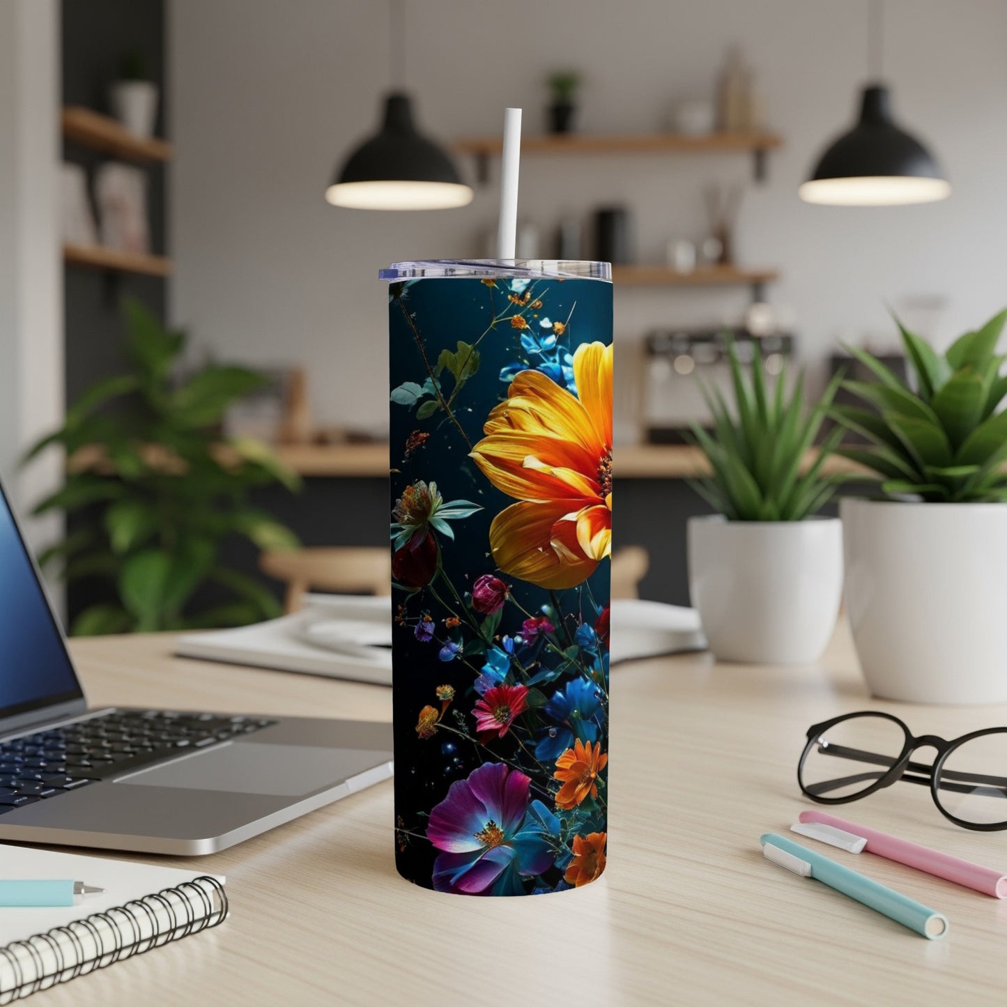 Tall tumbler with vibrant floral design on a desk next to a laptop.