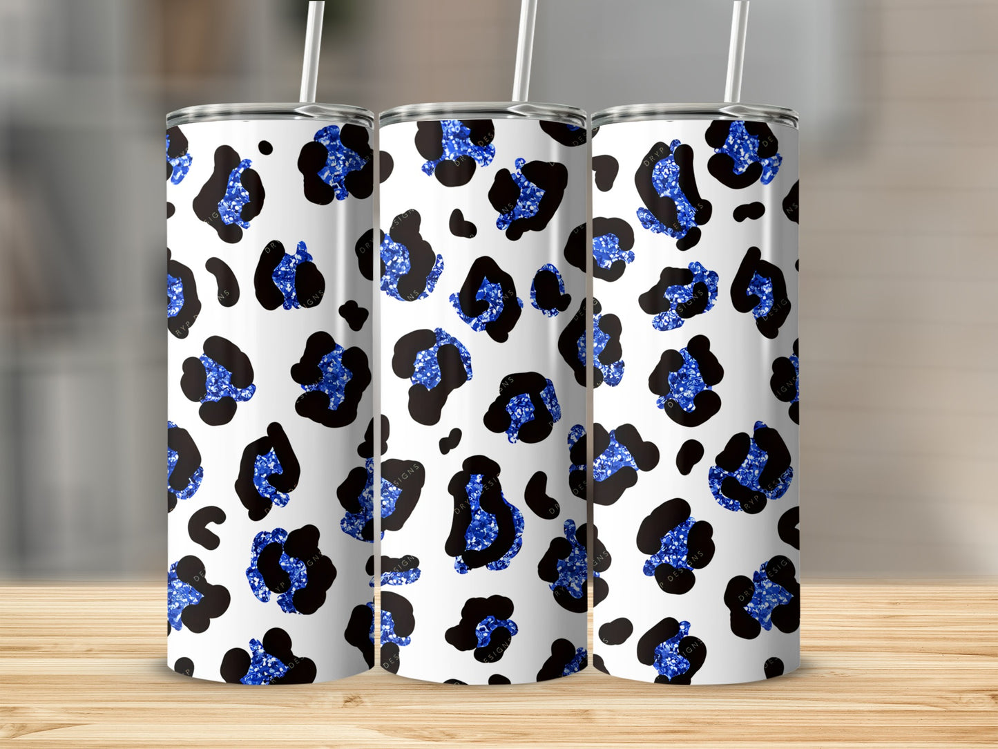 Three tumblers with blue leopard print glitter on a wooden surface.