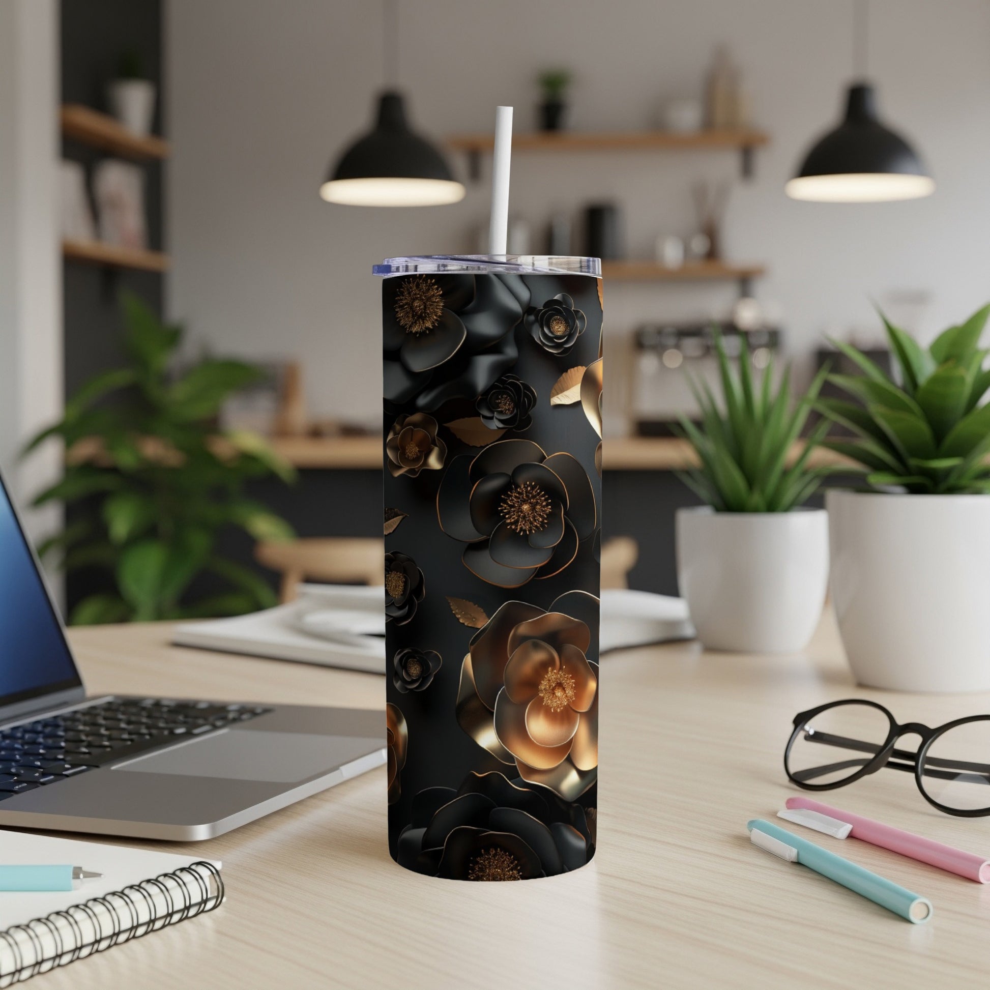 Black floral tumbler with gold accents, straw, on a desk with a laptop.