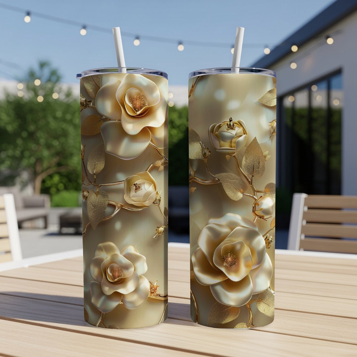 Two gold-toned floral tumblers with straws on a table.