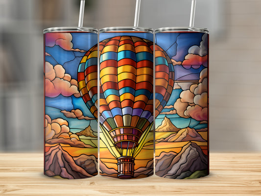 Stained glass hot air balloon graphic on three tumblers against a mountain landscape.