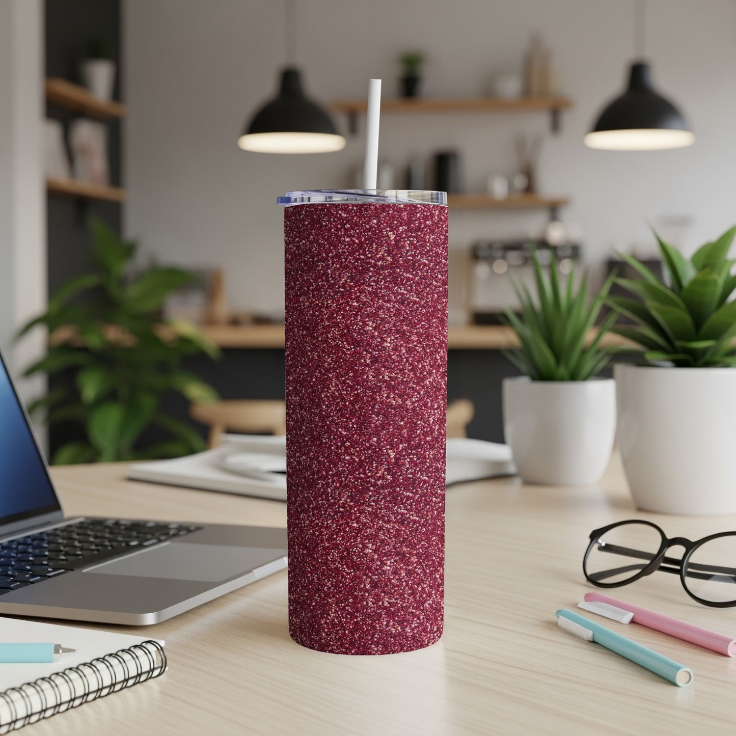 Glittery burgundy tumbler with straw on a desk with laptop and glasses.