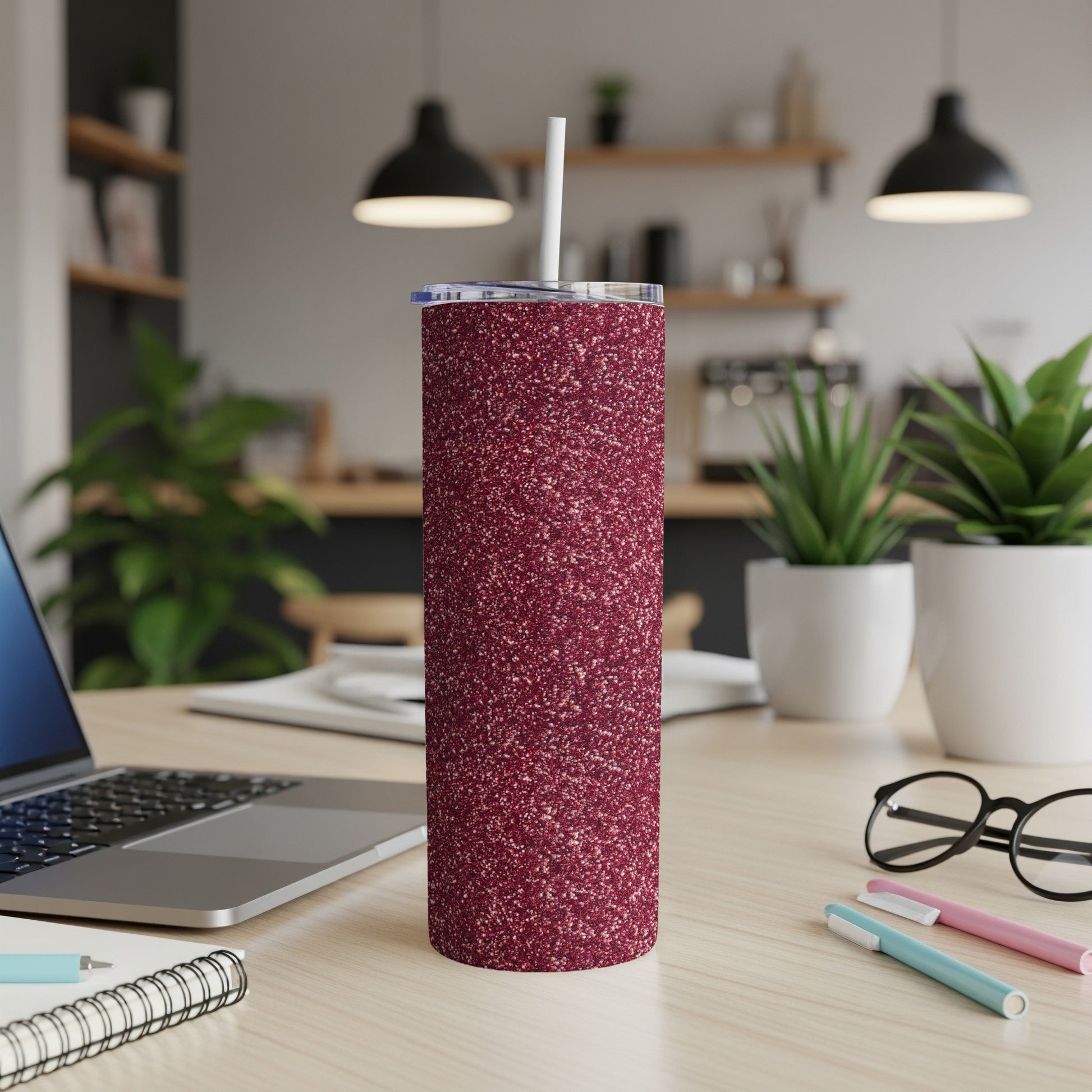 Glittery burgundy tumbler with straw on a desk with laptop and glasses.