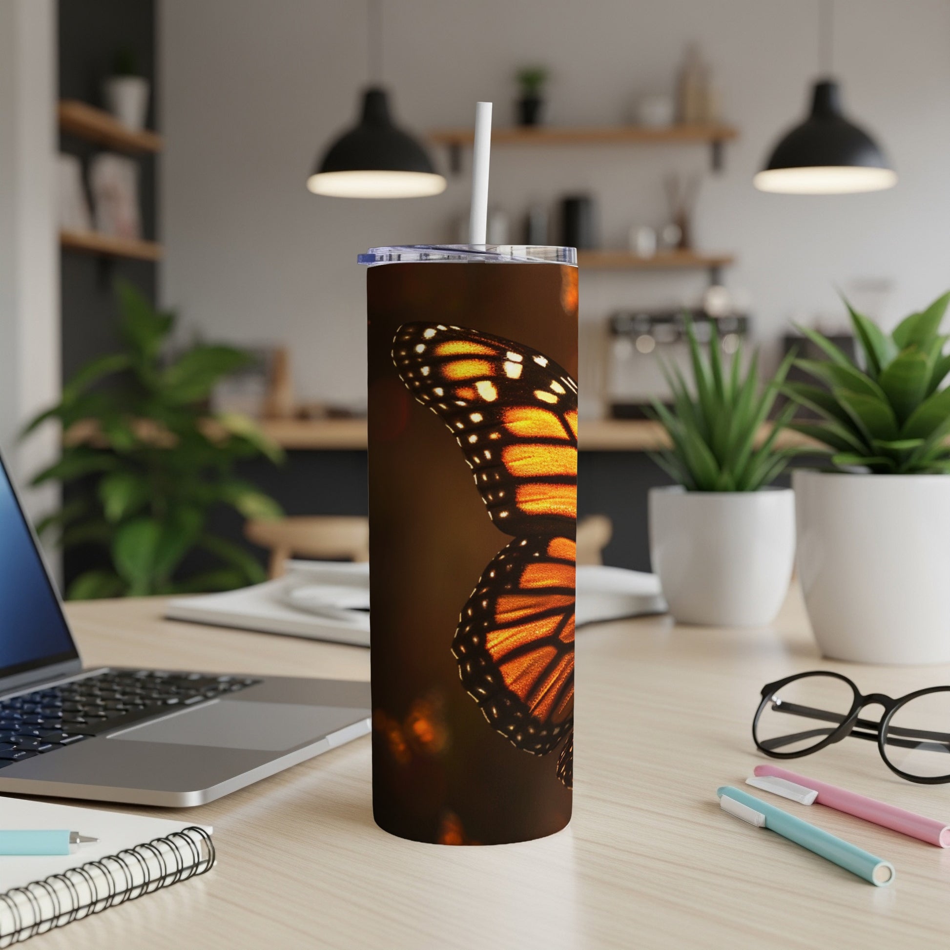 Monarch butterfly wings on a tall, skinny tumbler with a straw.