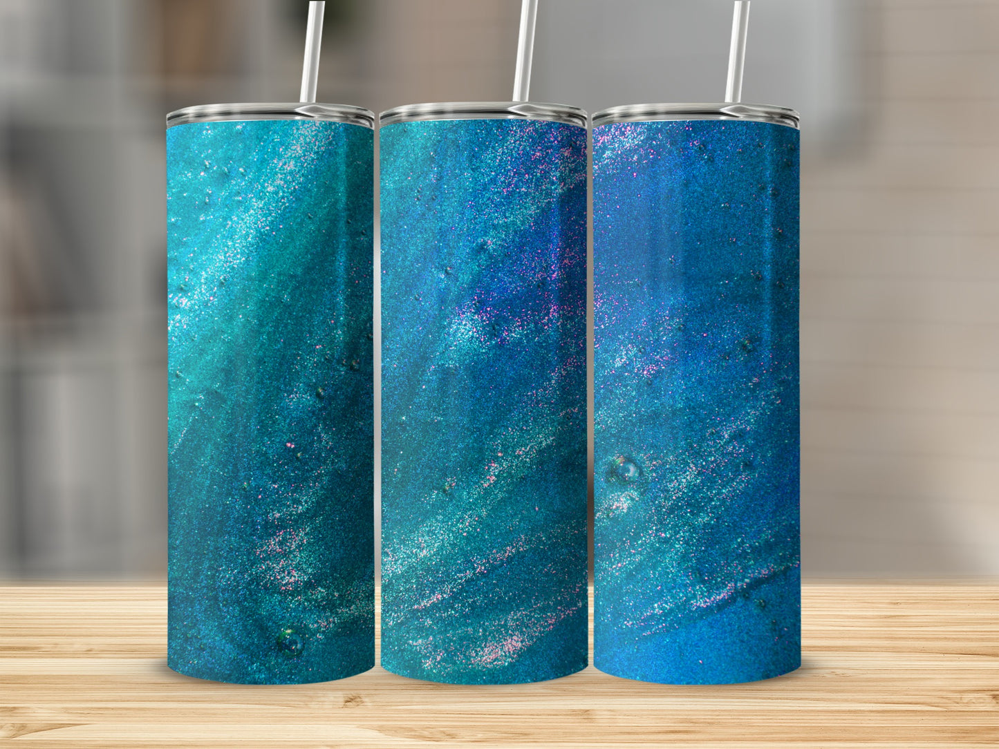 Three blue and teal glitter tumblers with straws on a wooden surface.