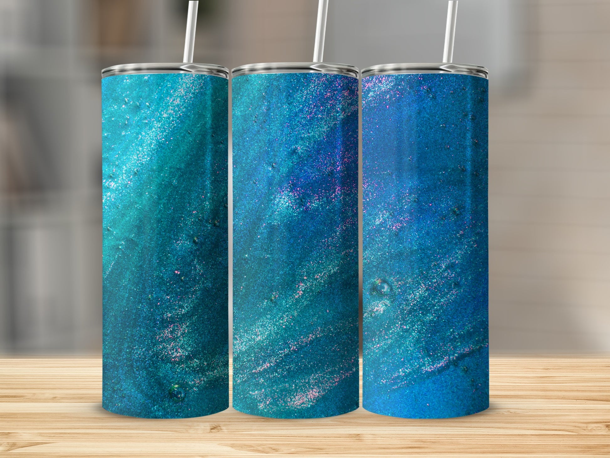 Three blue and teal glitter tumblers with straws on a wooden surface.