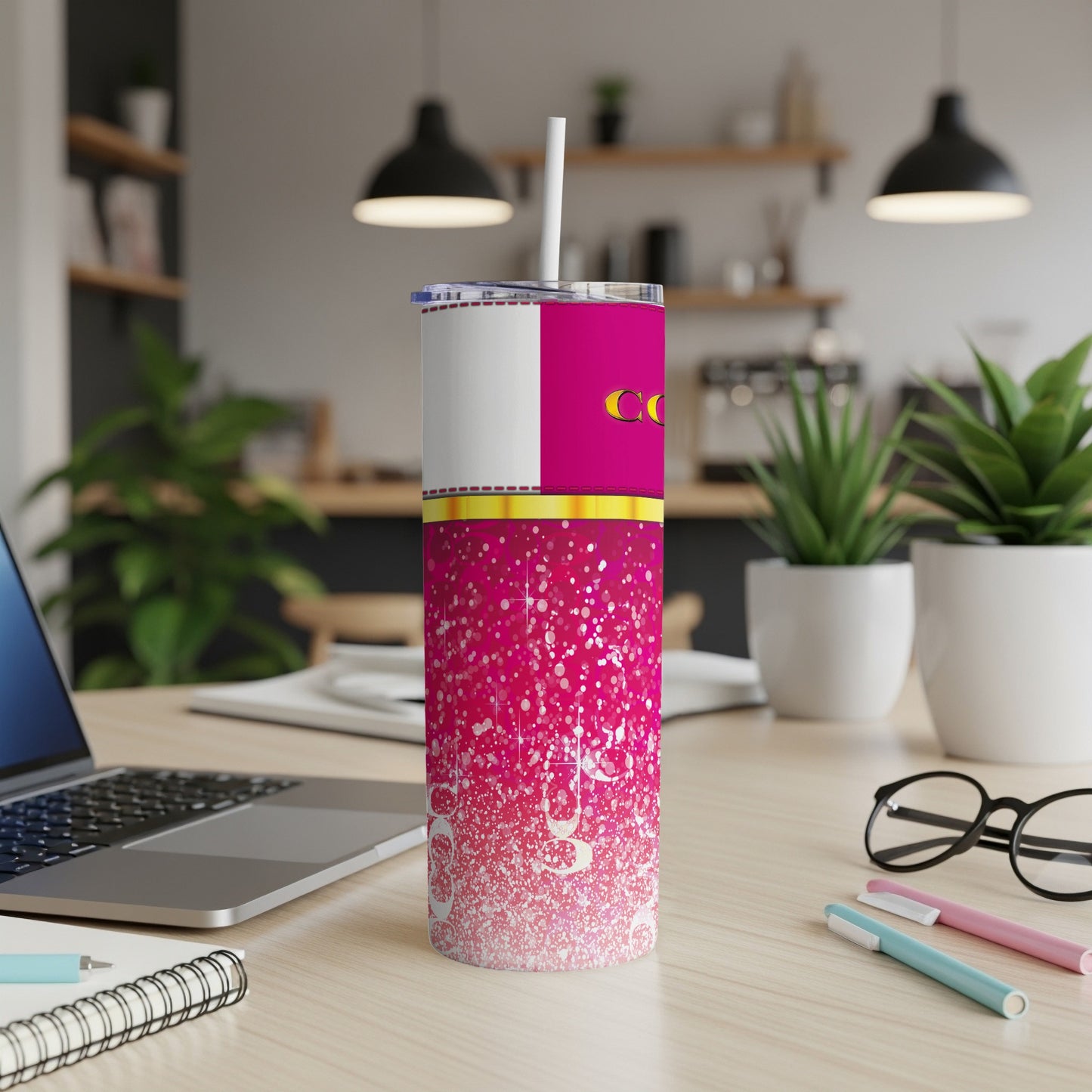 Pink tumbler with white and gold accents, straw, laptop, and glasses on a desk.