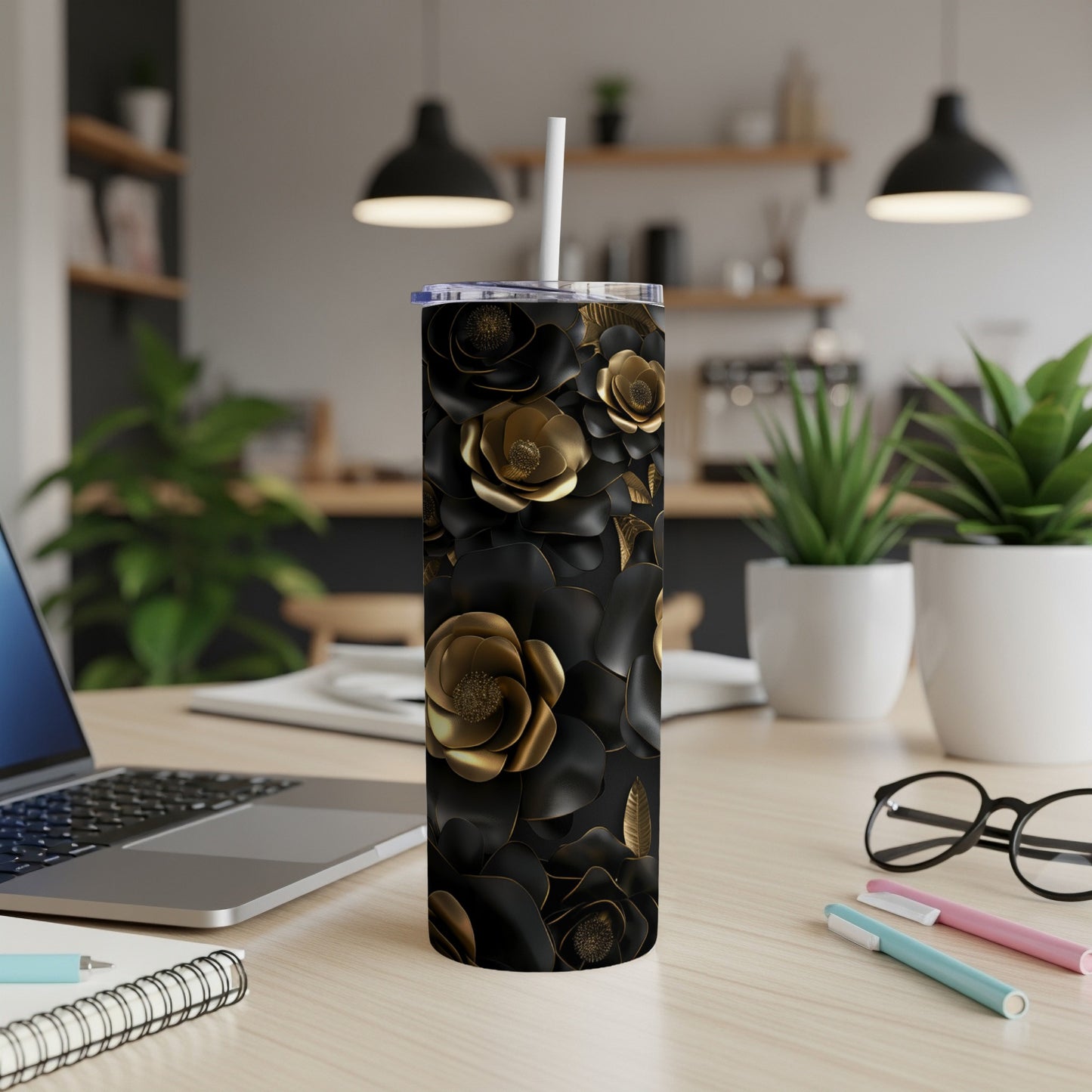 Black tumbler with gold floral pattern, straw, on a desk.
