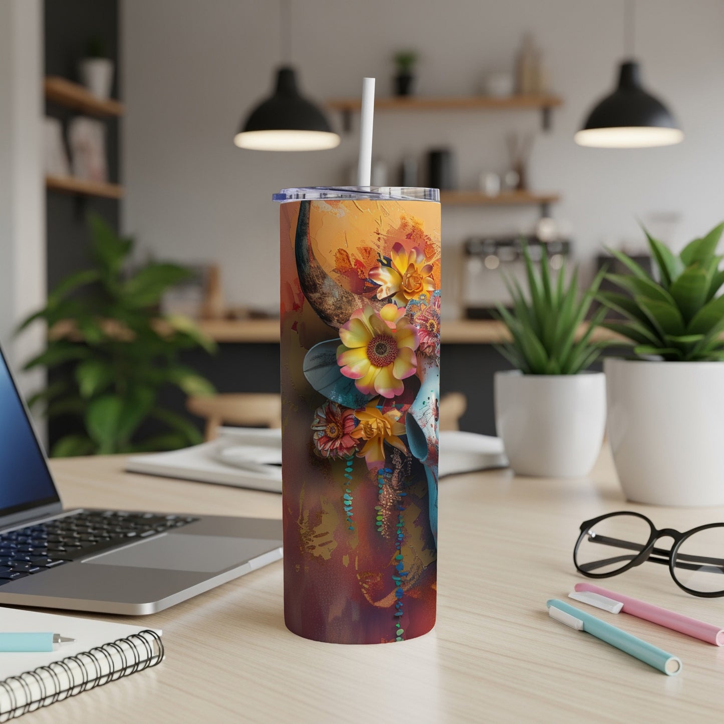 Tall tumbler with a floral skull design, on a desk with a laptop.