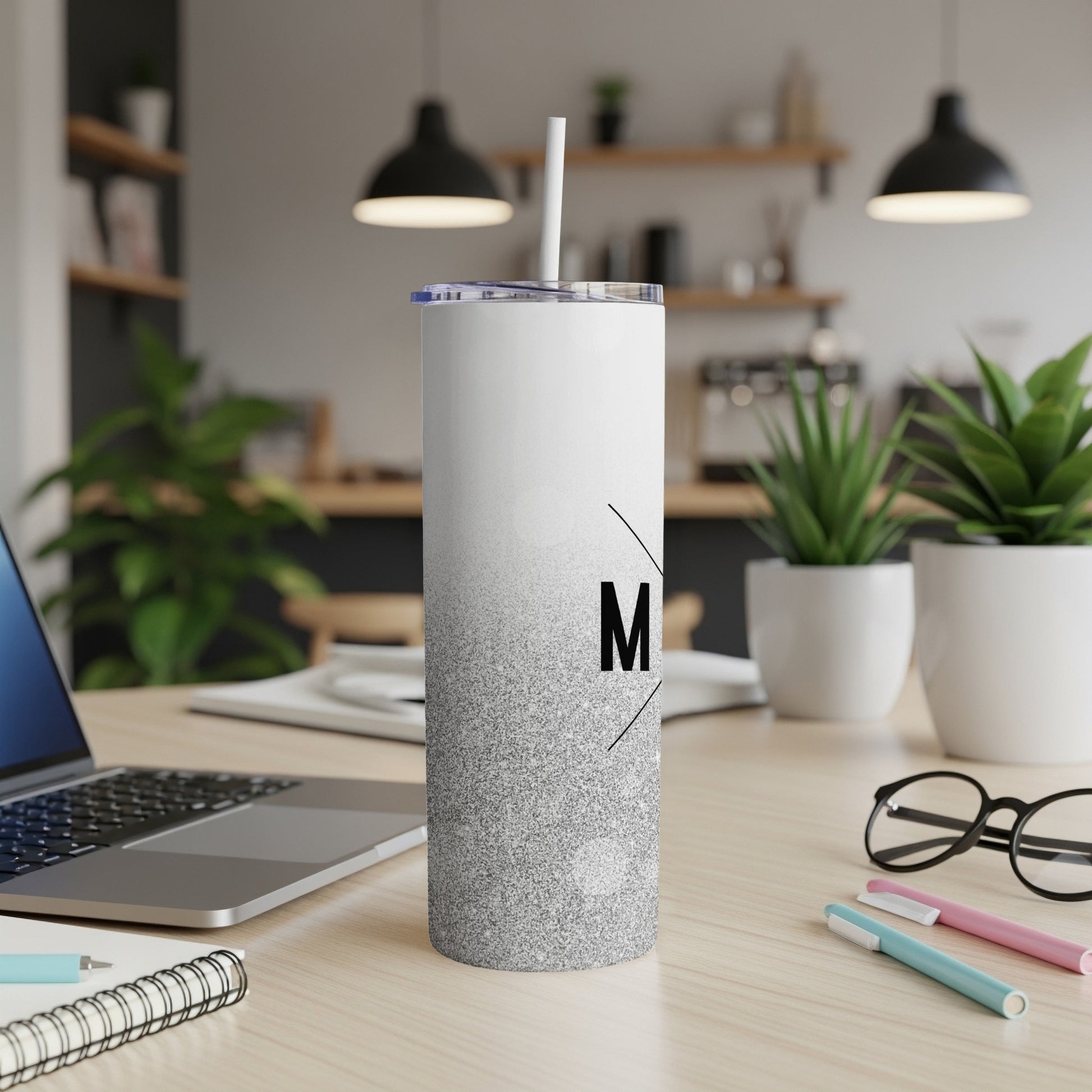 White and silver gradient tumbler with an "M" monogram, on a desk.