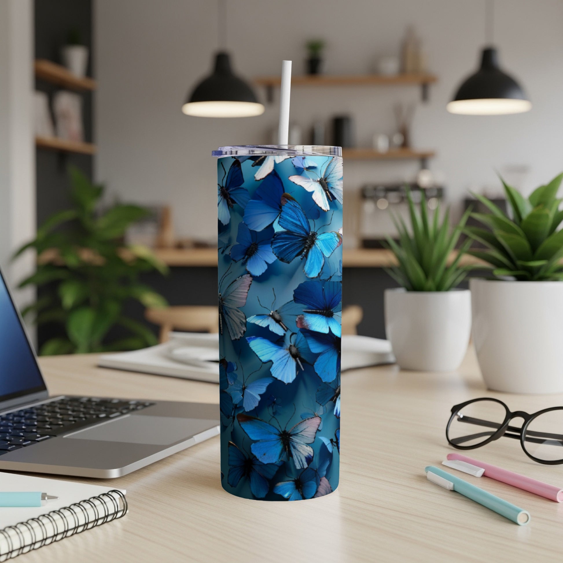 Blue butterfly patterned insulated tumbler with straw on desk.