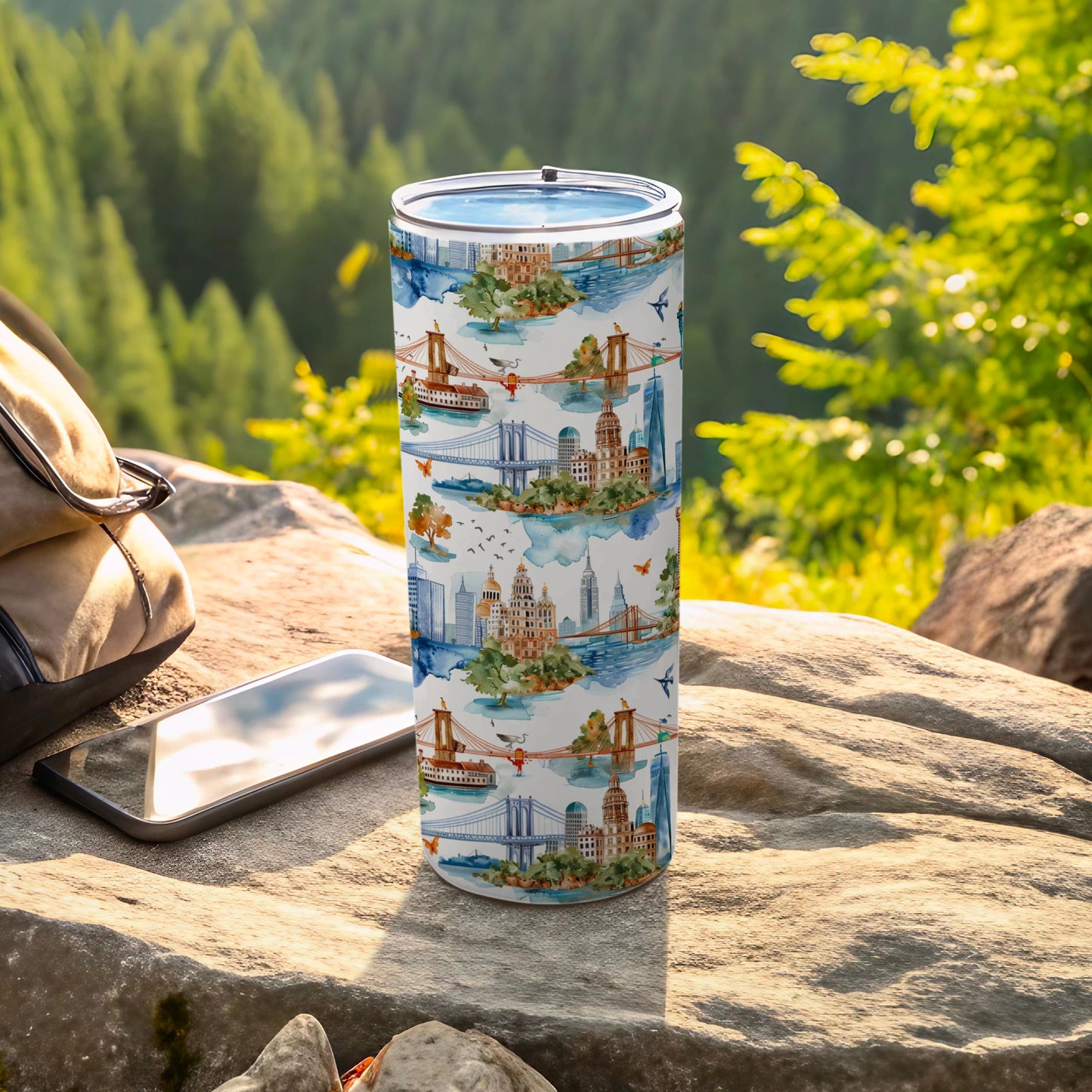 Tumbler with watercolor New York City skyline pattern, outdoors on rocks.