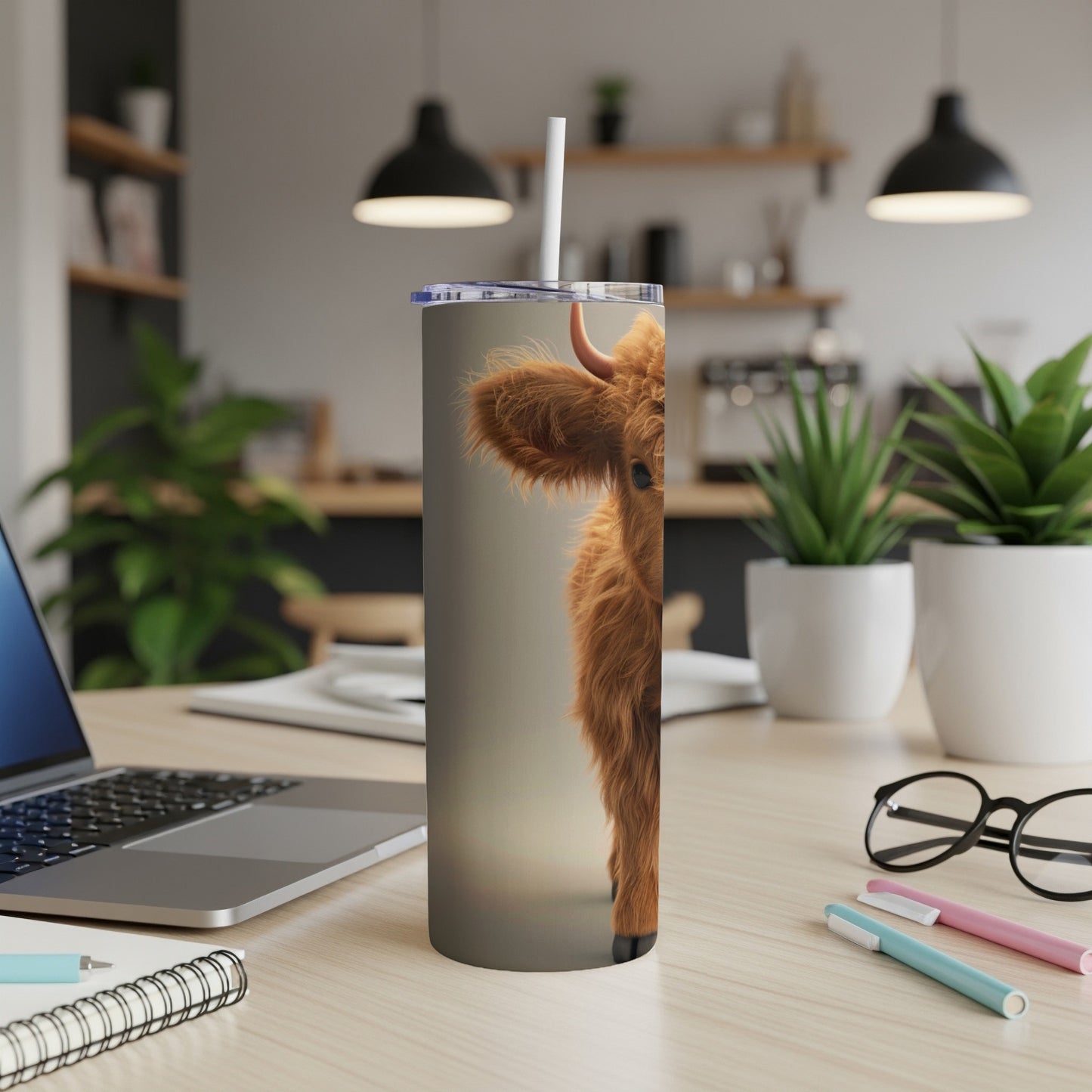 Close up of a fluffy Highland cow peeking around a stainless steel tumbler.