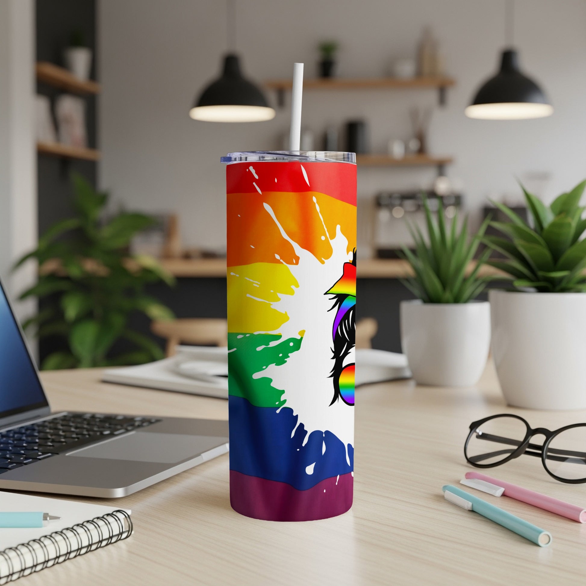 Rainbow gradient tumbler with white unicorn head illustration on a desk.