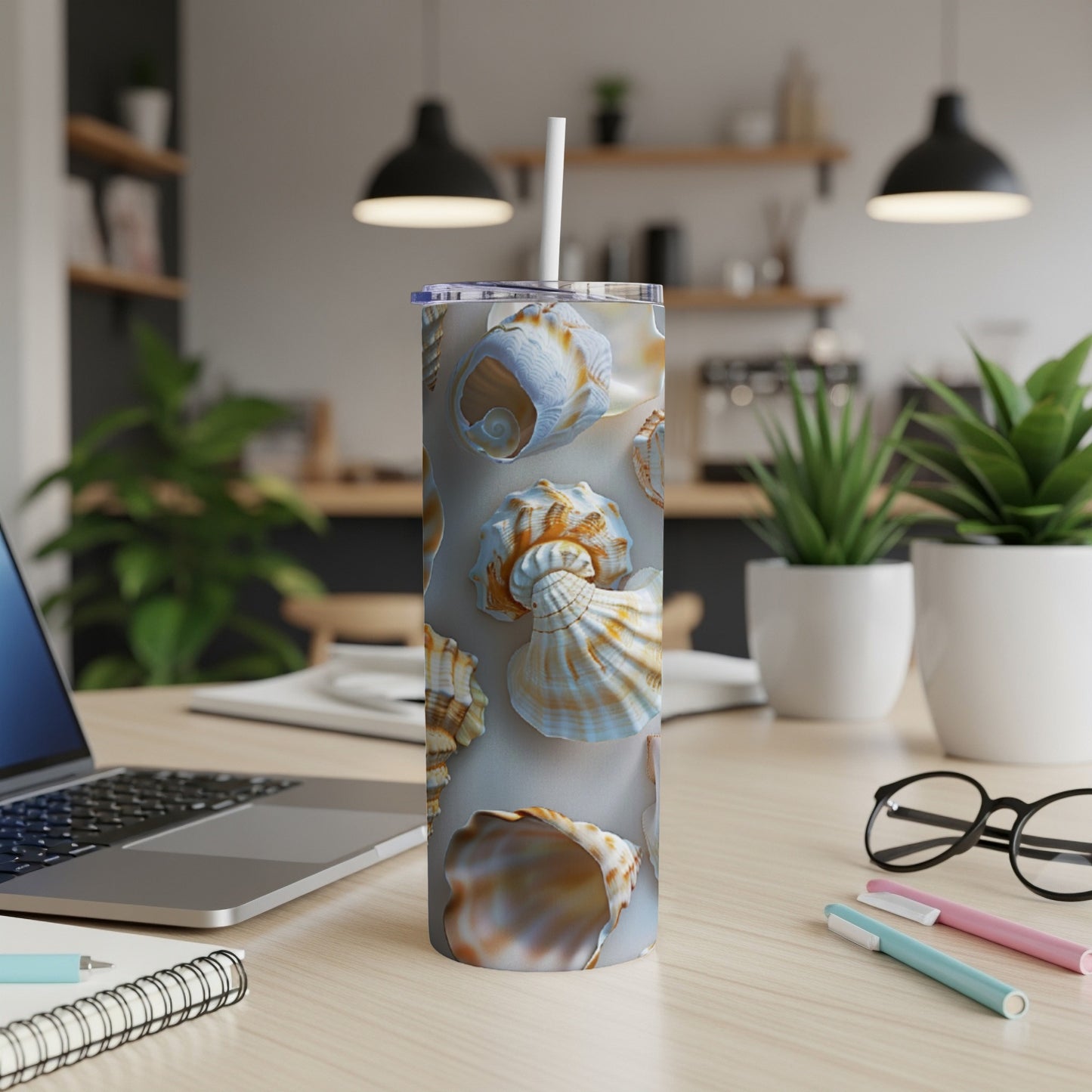 Seashell pattern on a white tumbler with a straw, on a desk.