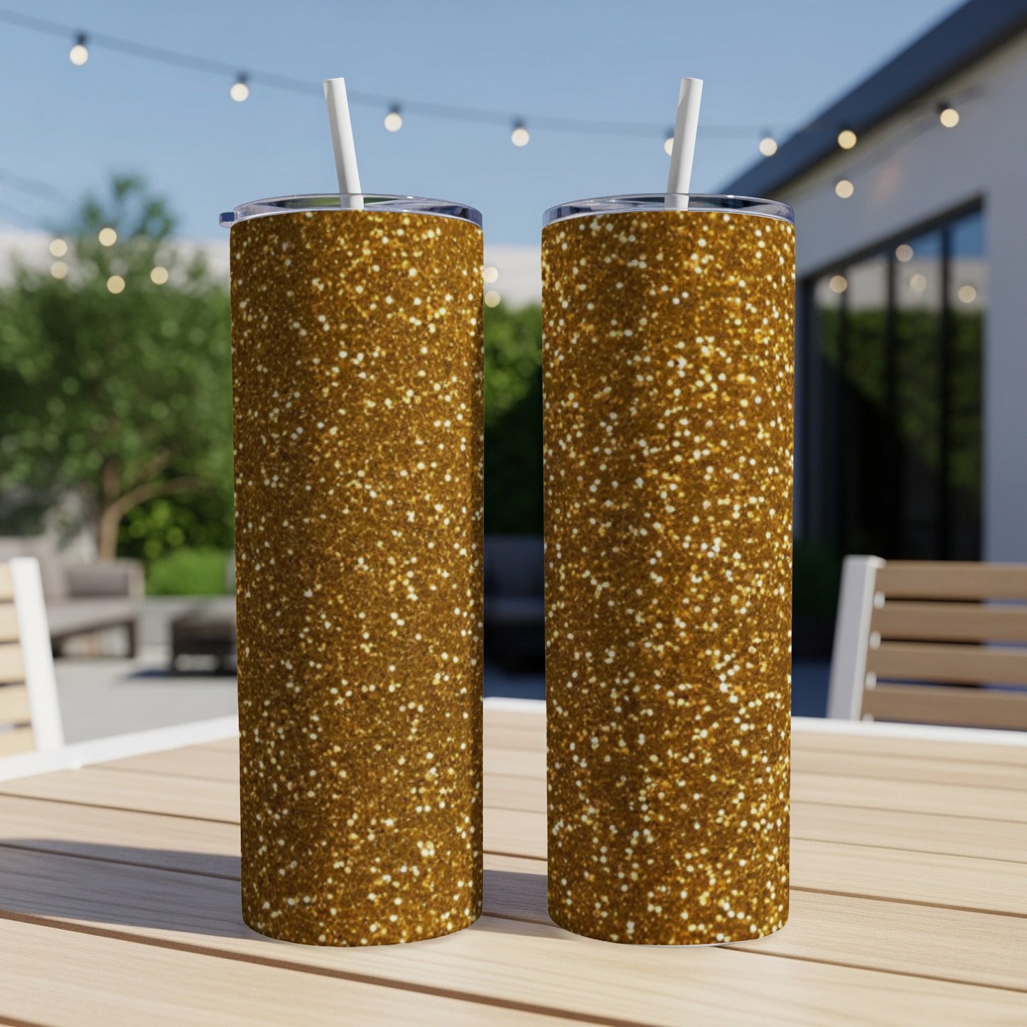 Two tall gold glitter tumblers with straws sit on a wooden table.
