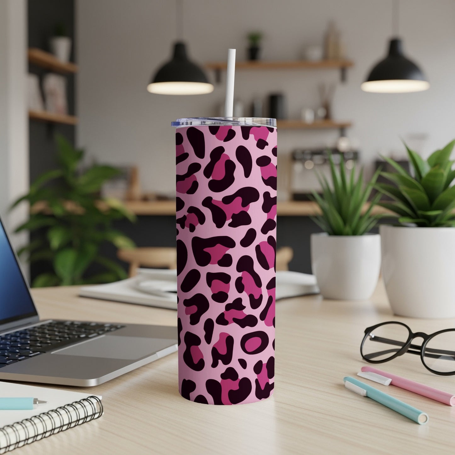 Pink leopard print tumbler with straw on a desk next to a laptop and notebooks.