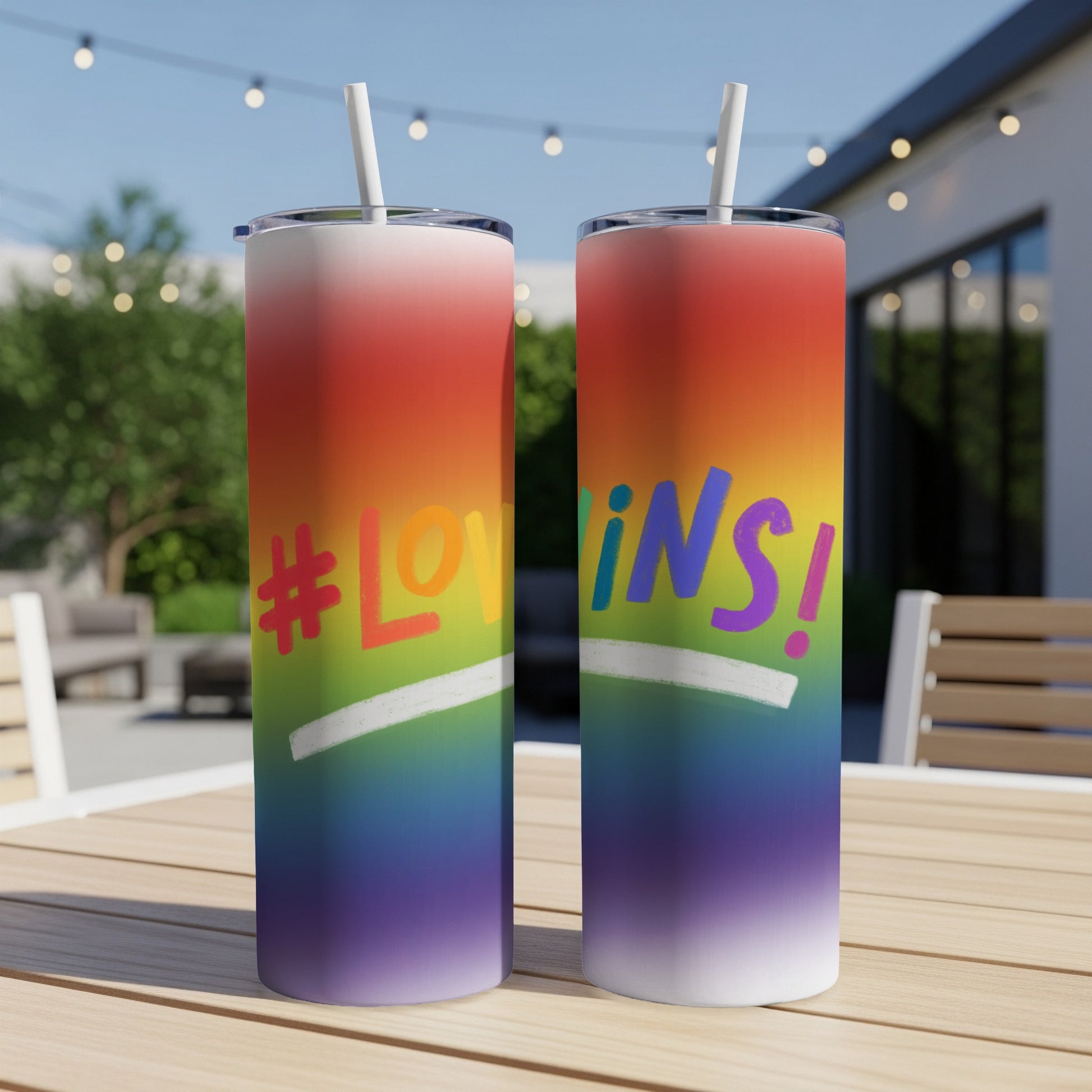 Two tumblers with rainbow gradient, `#LOVING!` text, on outdoor table.