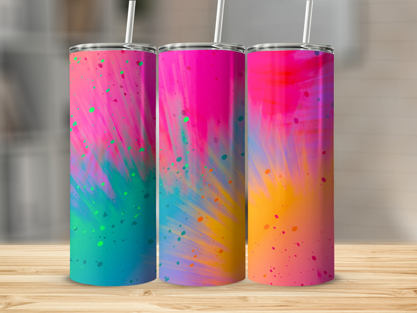 Three tumblers with colorful abstract splatter patterns and straws on a wooden table.
