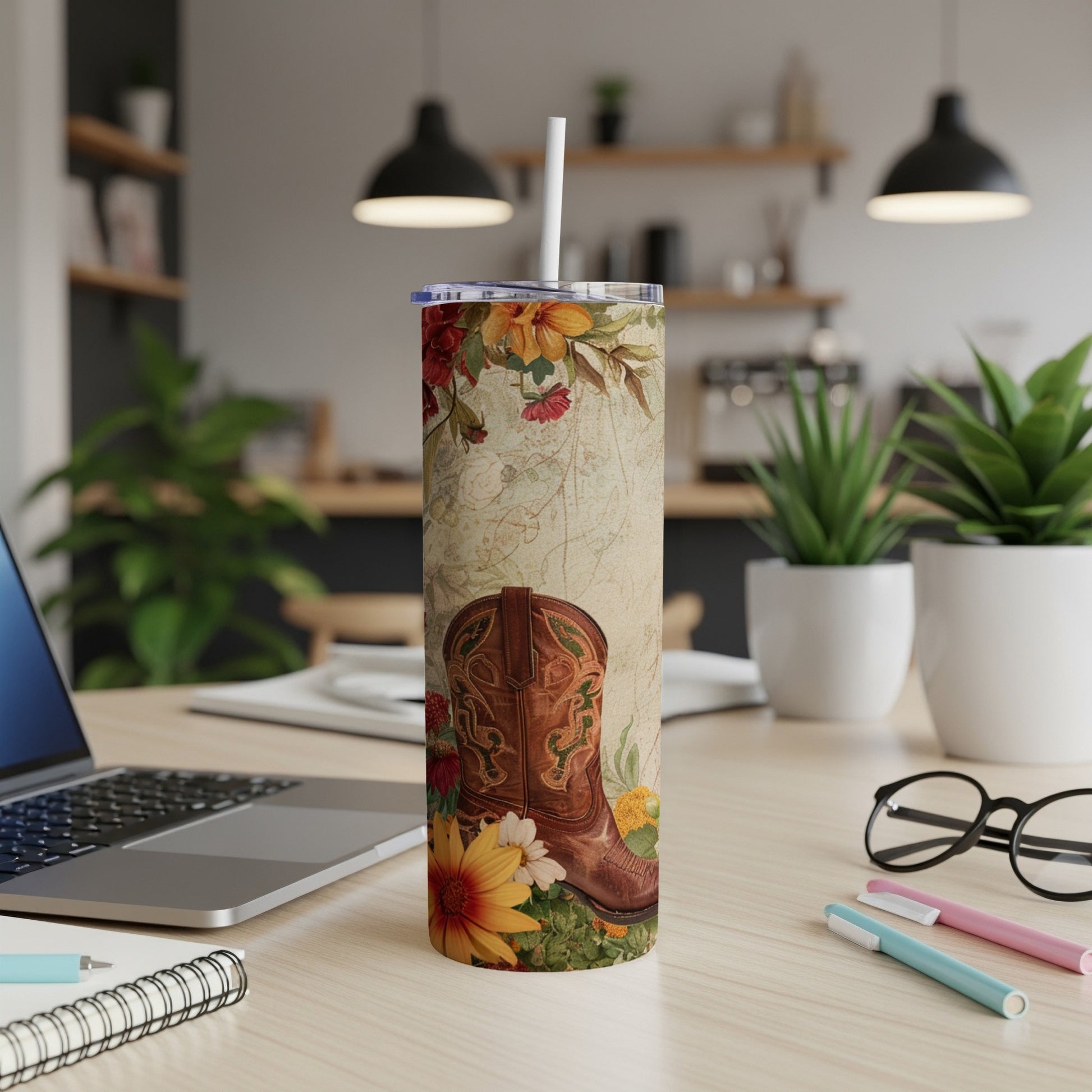 Cowboy boot and floral design on a tumbler with straw, on a desk.