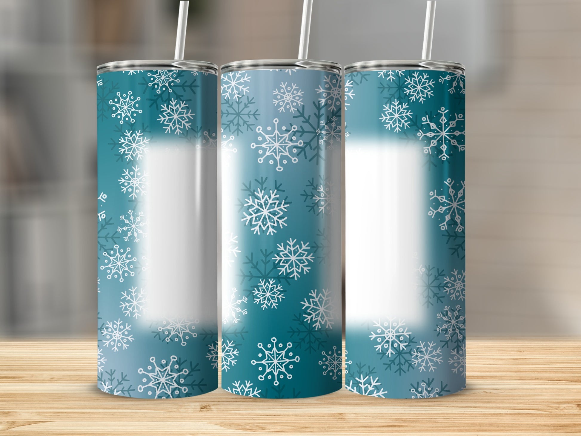 Three teal tumblers with white snowflake patterns stand on a wooden surface.