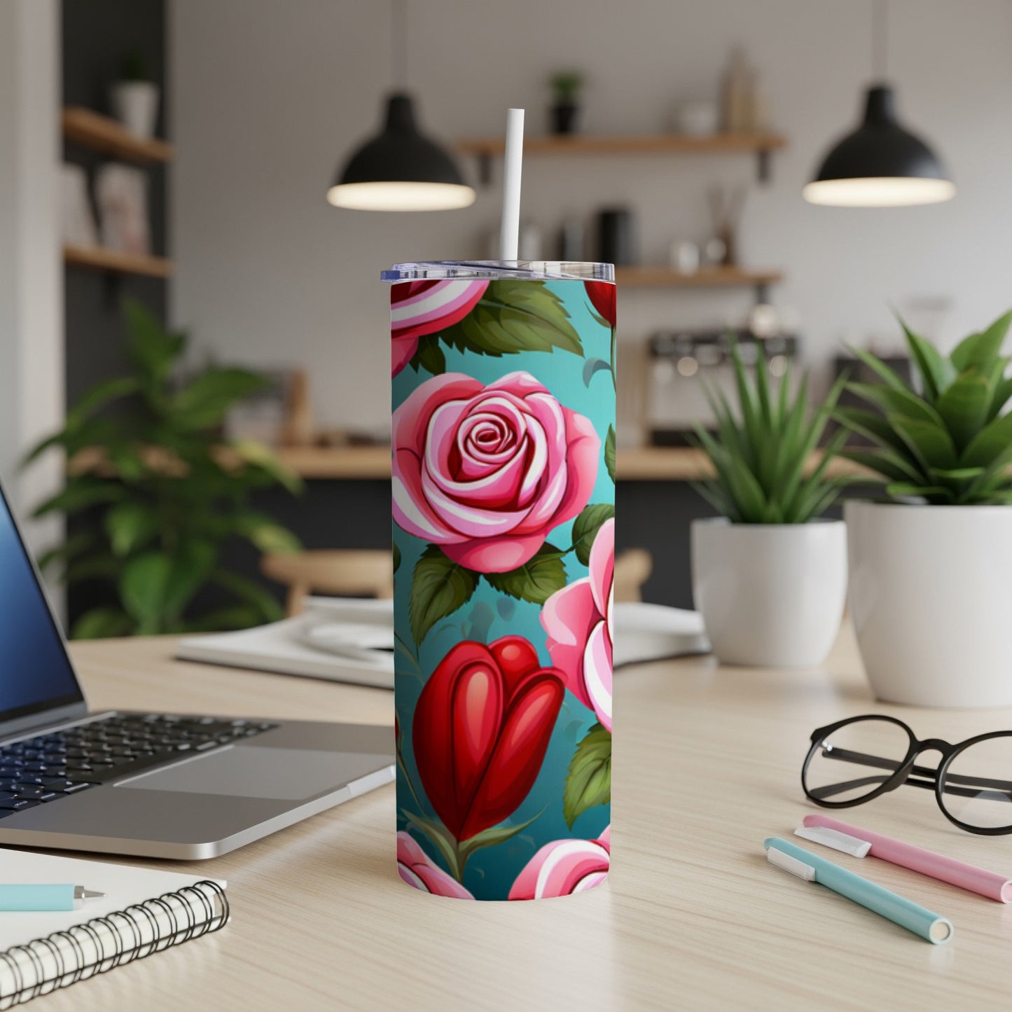 Turquoise tumbler with red and pink roses and tulips, on a desk.
