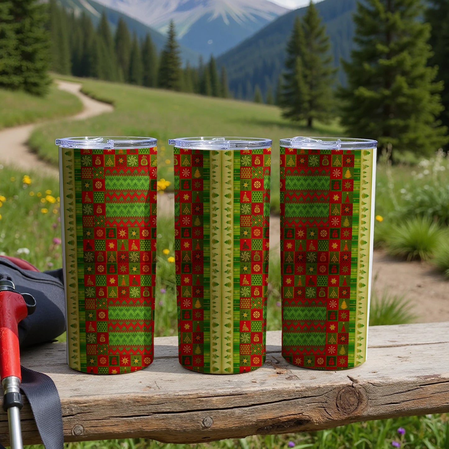 Three tall tumblers with a green and red Christmas sweater pattern on a wooden surface.