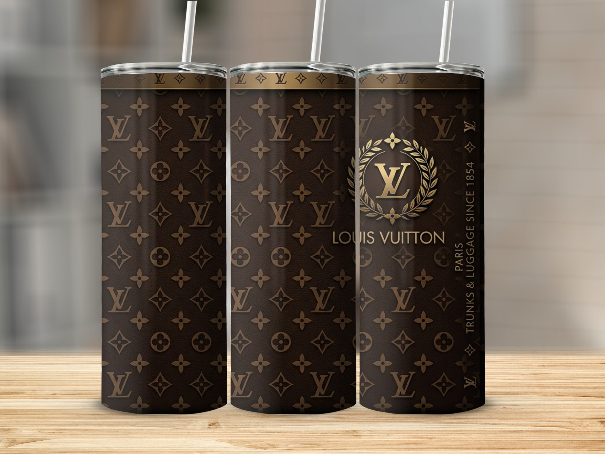 Three Louis Vuitton pattern tumblers with straws on a wooden surface.