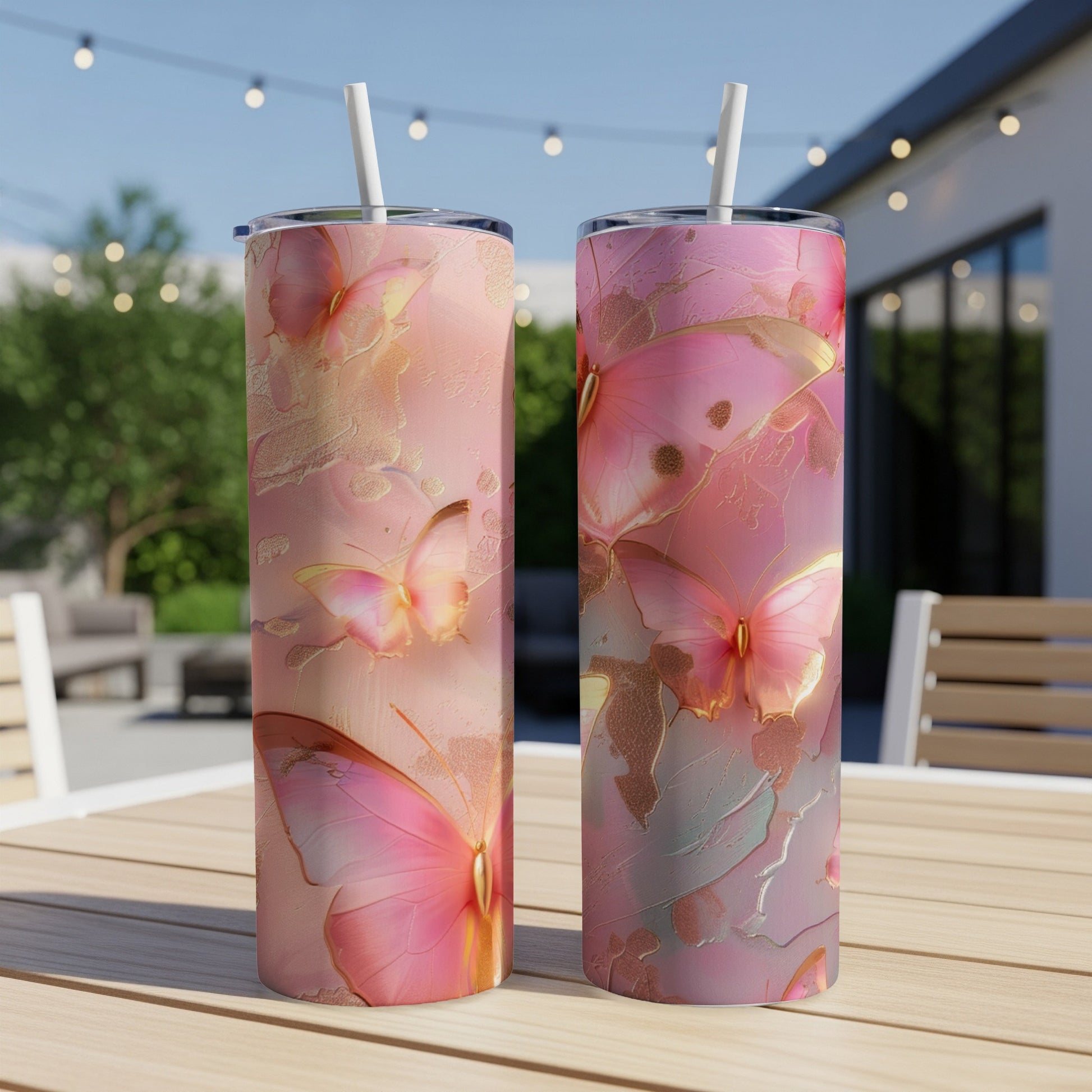 Two pink tumblers with butterfly and floral designs on an outdoor table.