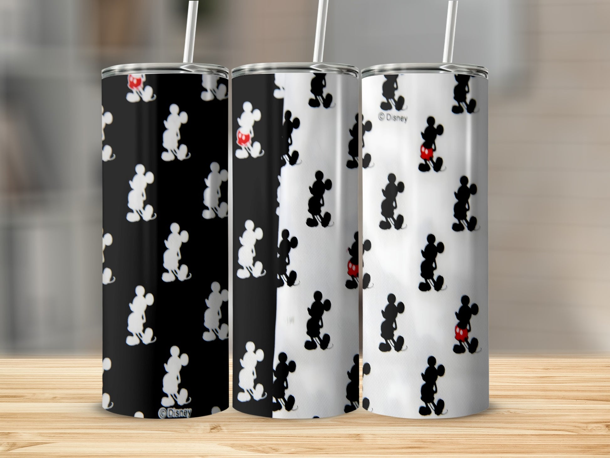 Three Disney Mickey Mouse tumblers with straws, patterned on black and white backgrounds.