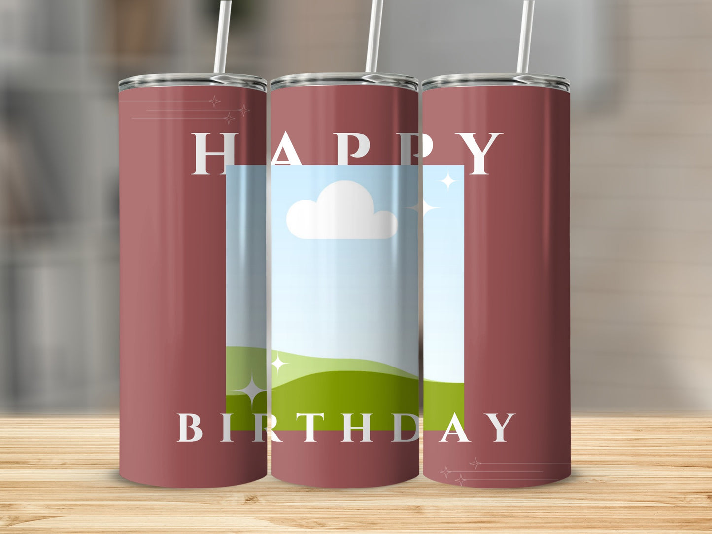Three maroon tumblers with "Happy Birthday" text and sky, cloud, and grassy hill graphic.