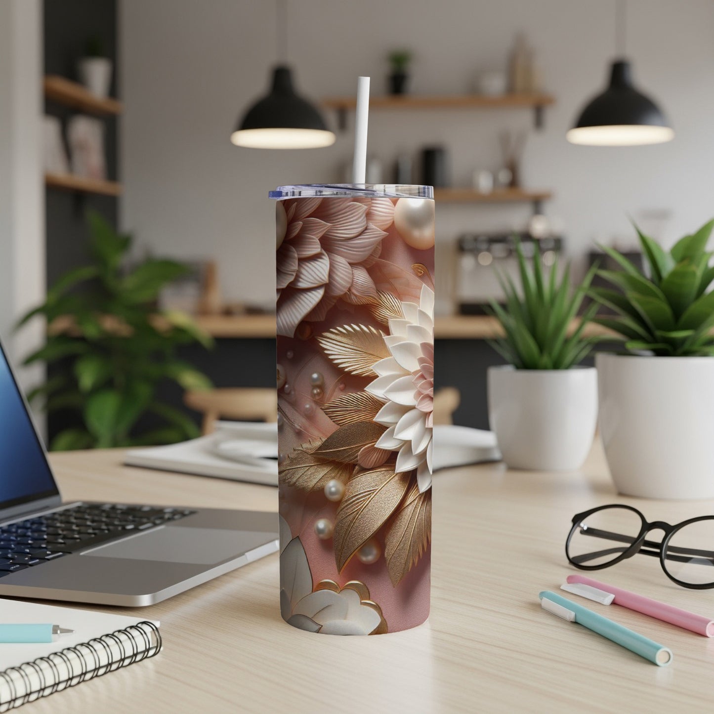 Floral patterned tumbler with straw on a desk, with a laptop and pens.