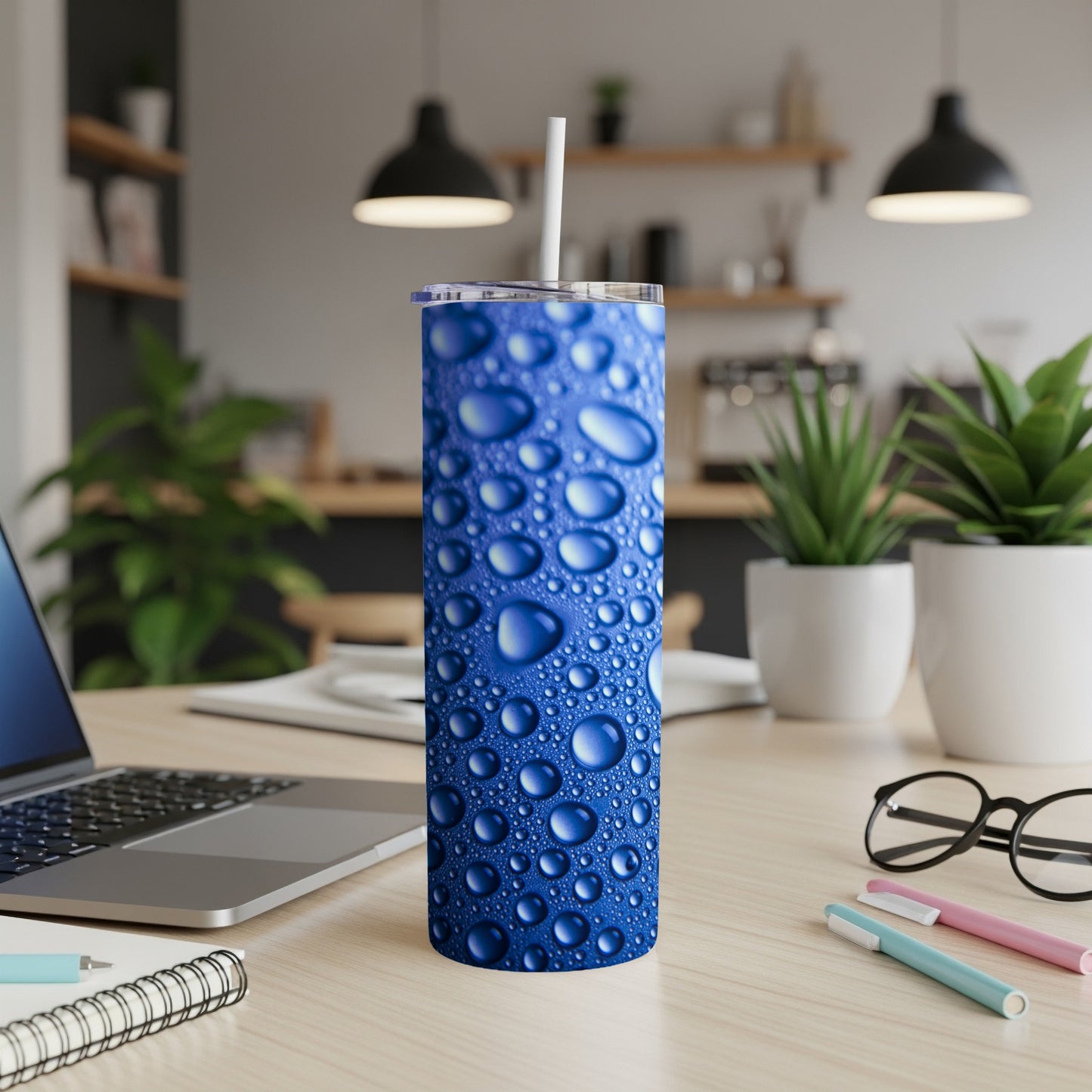 Blue tumbler with water droplet pattern on desk with laptop and pens.
