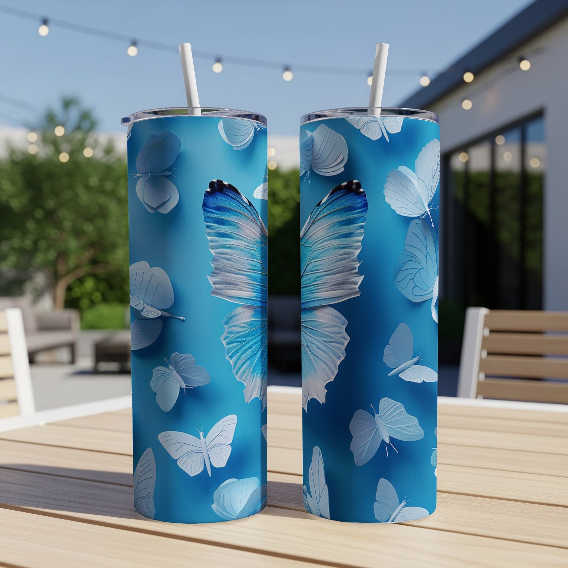 Two blue tumblers with a white butterfly pattern on an outdoor table.