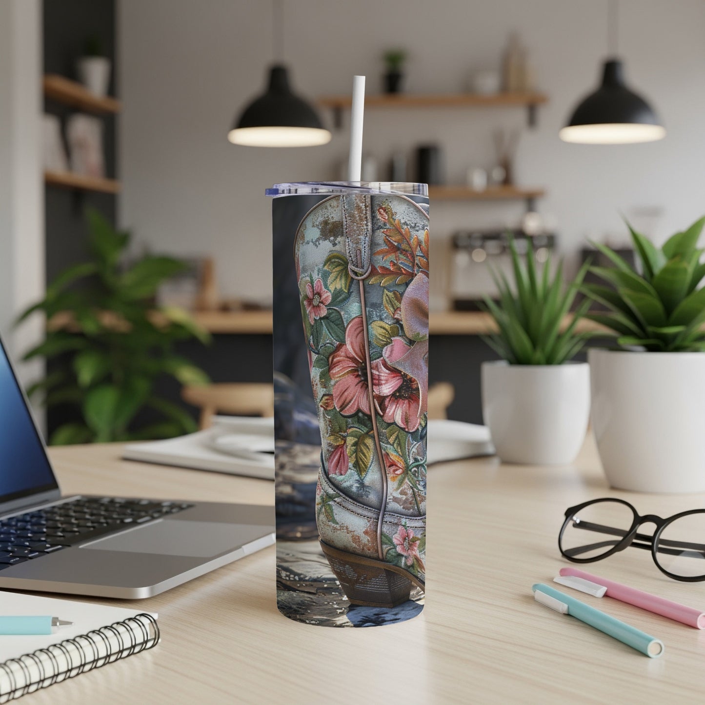 Cowboy boot tumbler with floral design and straw on a desk.