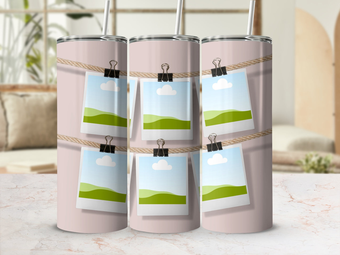 Three pink tumblers with photos of rolling hills and sky clipped to a string.