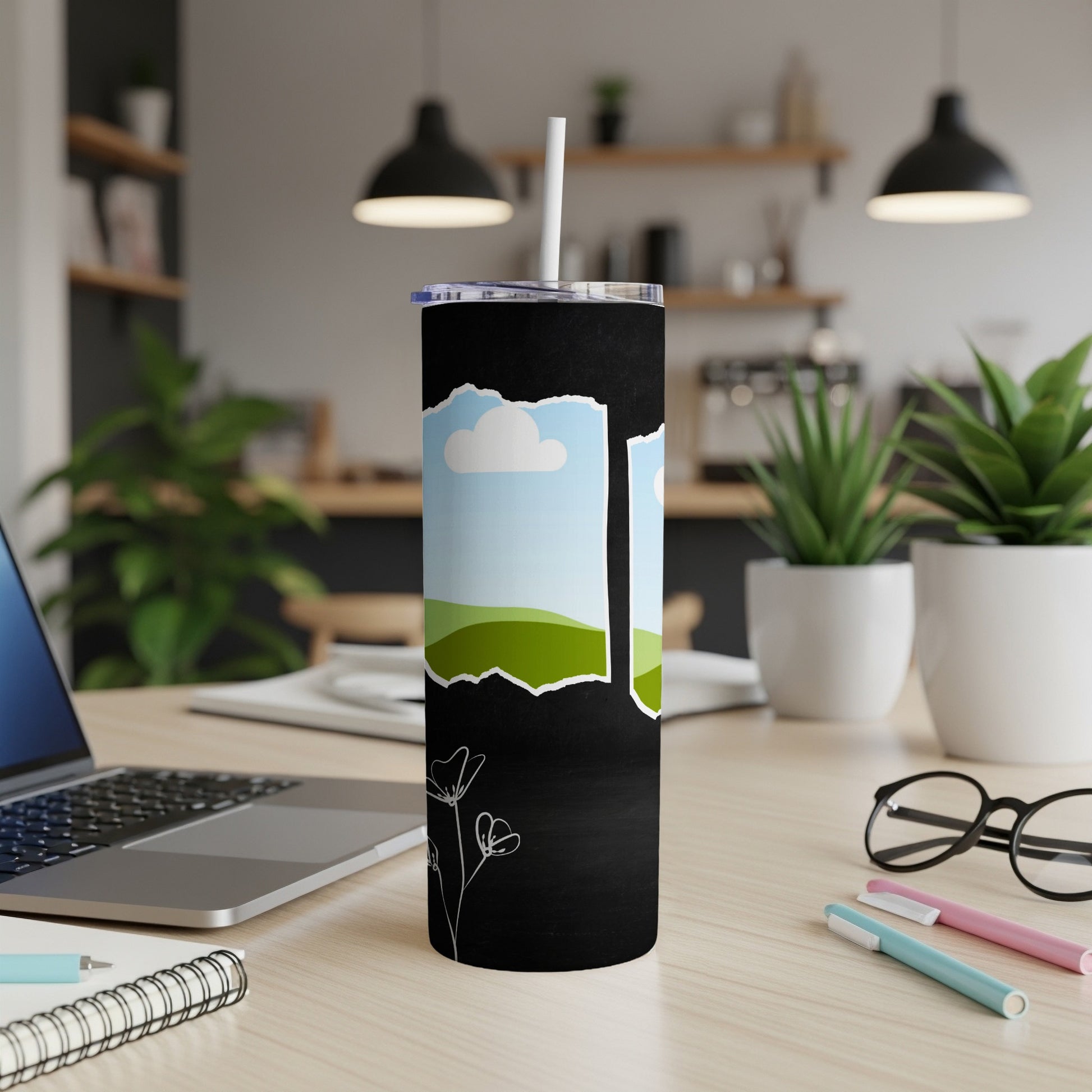 Black tumbler with torn paper graphic featuring landscape and clouds, with white flower line art.