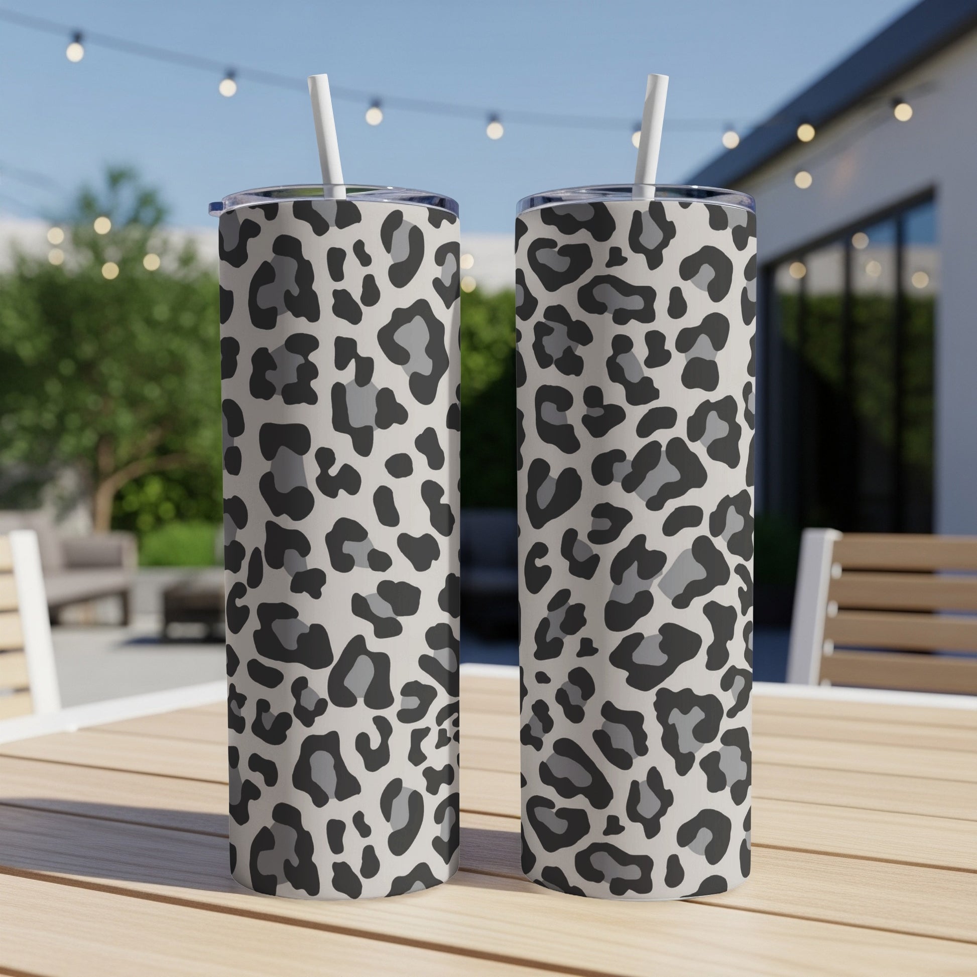 Two tall tumblers with a grey and black leopard print pattern sit on a wooden table outdoors.