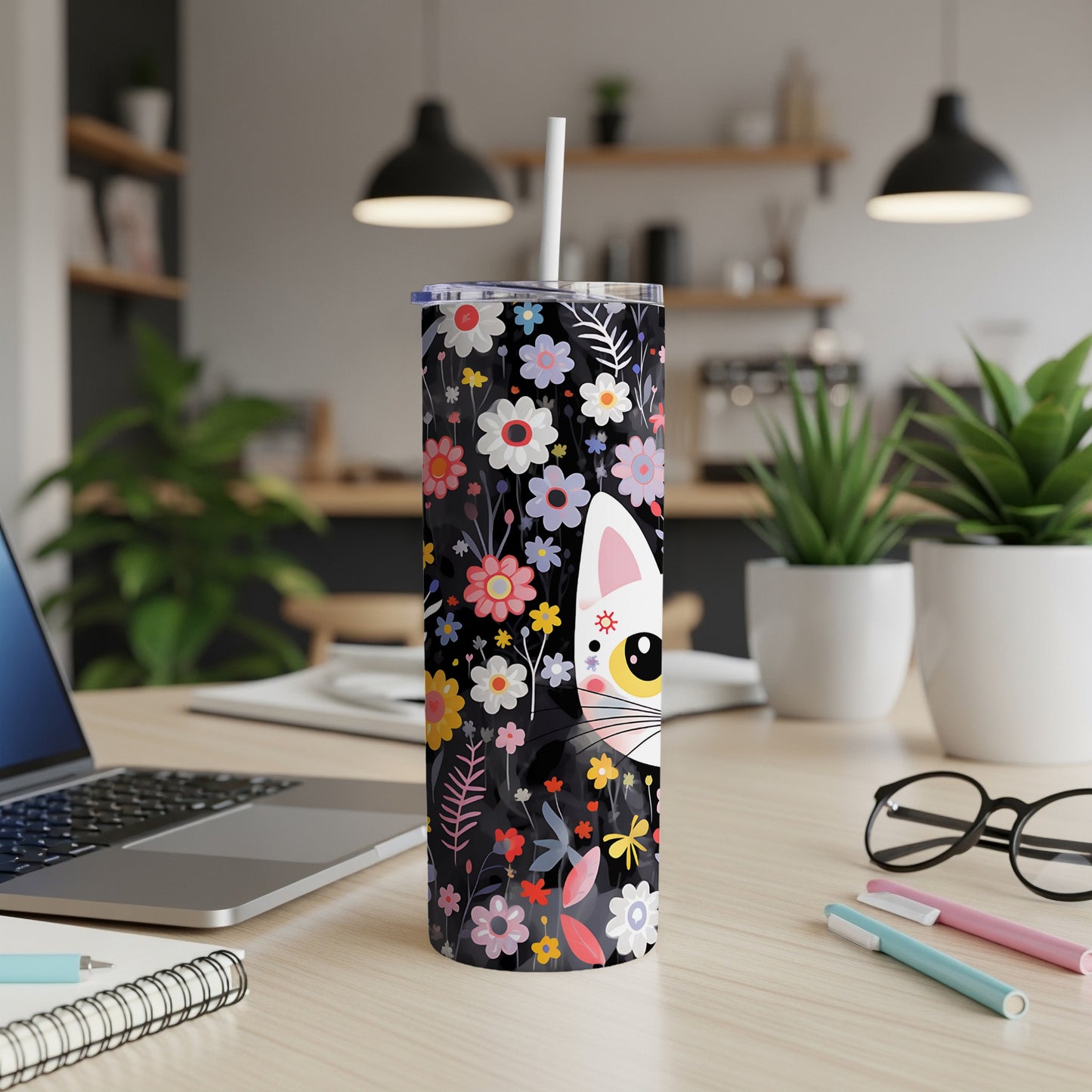 Black tumbler with white cat and colorful floral pattern, on a desk.