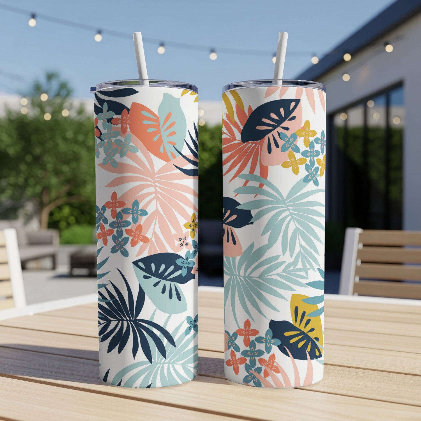 Two tropical floral print tumblers with straws on a table.