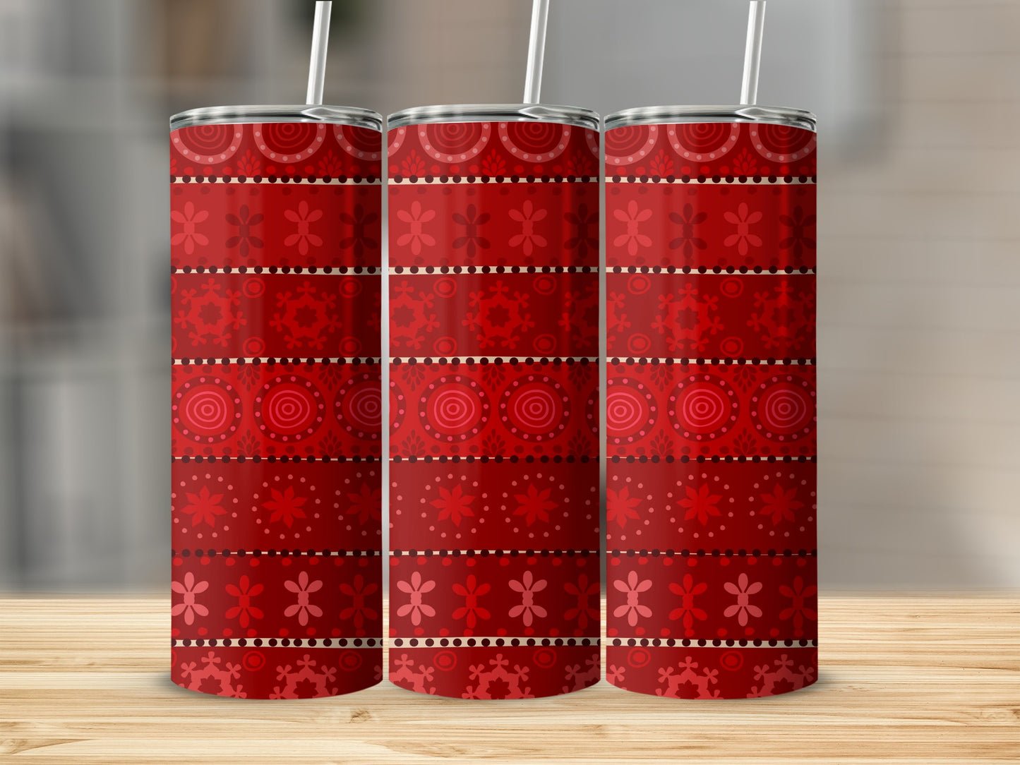 Three red patterned tumblers with straw on wooden surface.