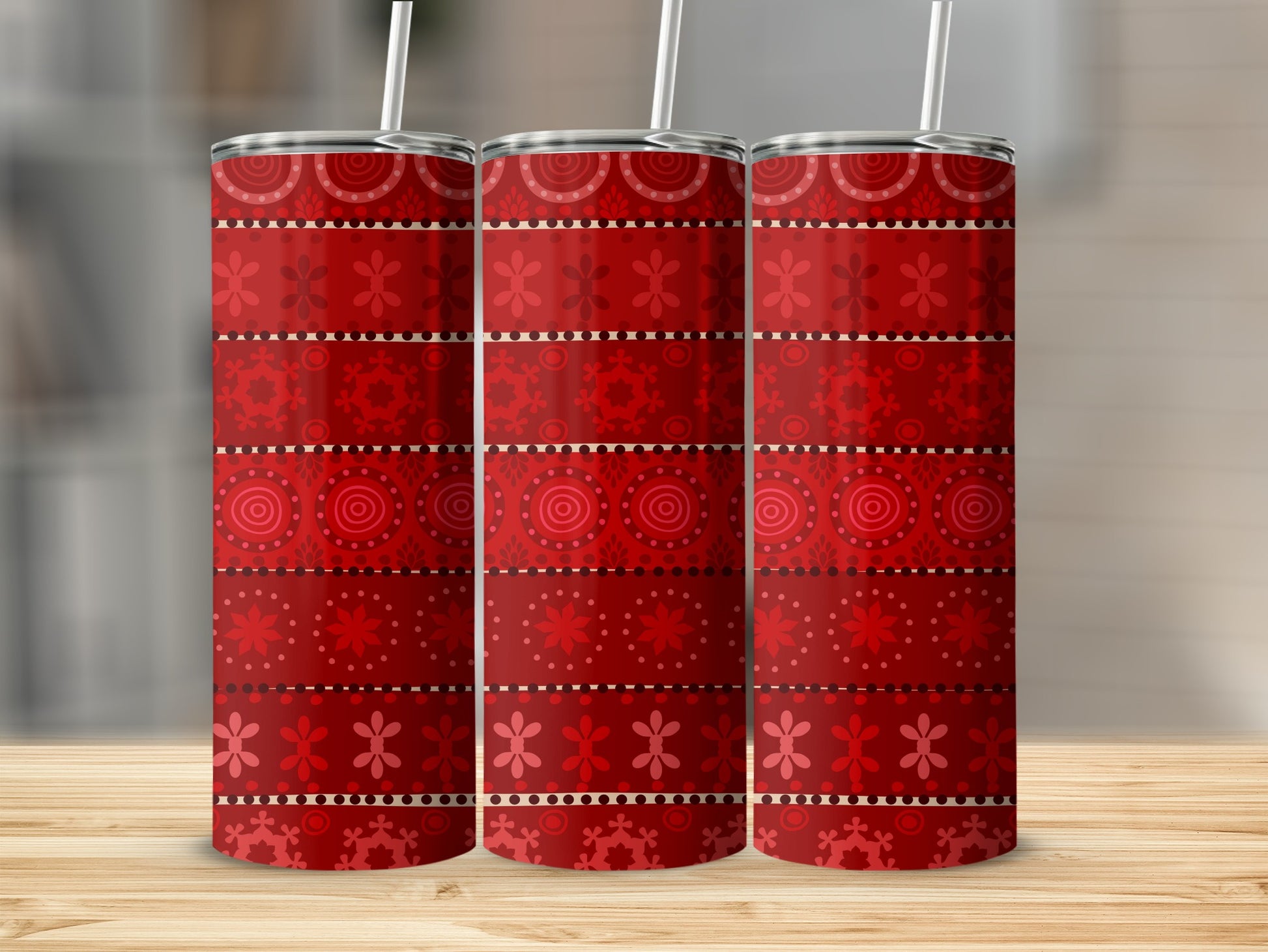 Three red patterned tumblers with straw on wooden surface.