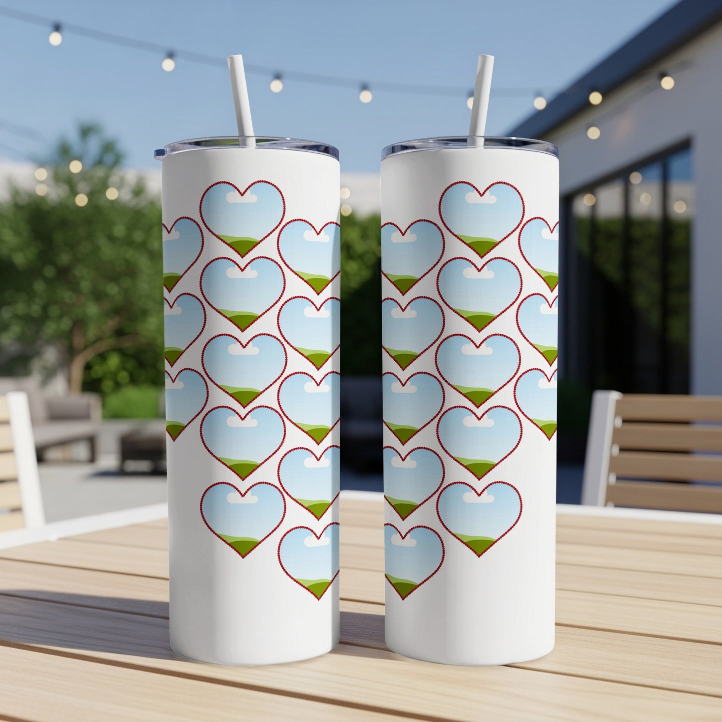 Two white tumblers with a repeating pattern of red-bordered heart shapes filled with a landscape of sky, clouds, and green hills.