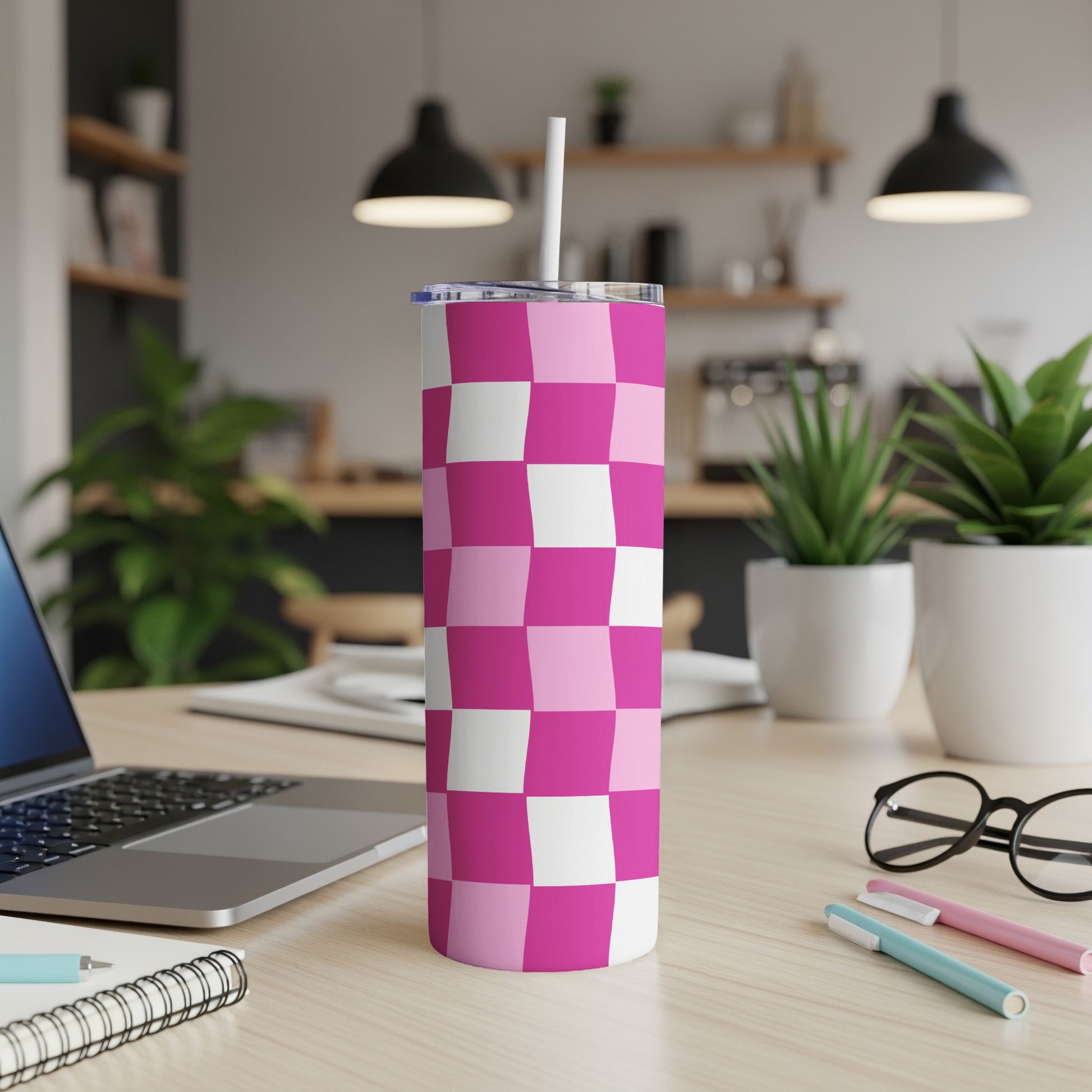 Pink and white checkered tumbler with a straw on a desk.