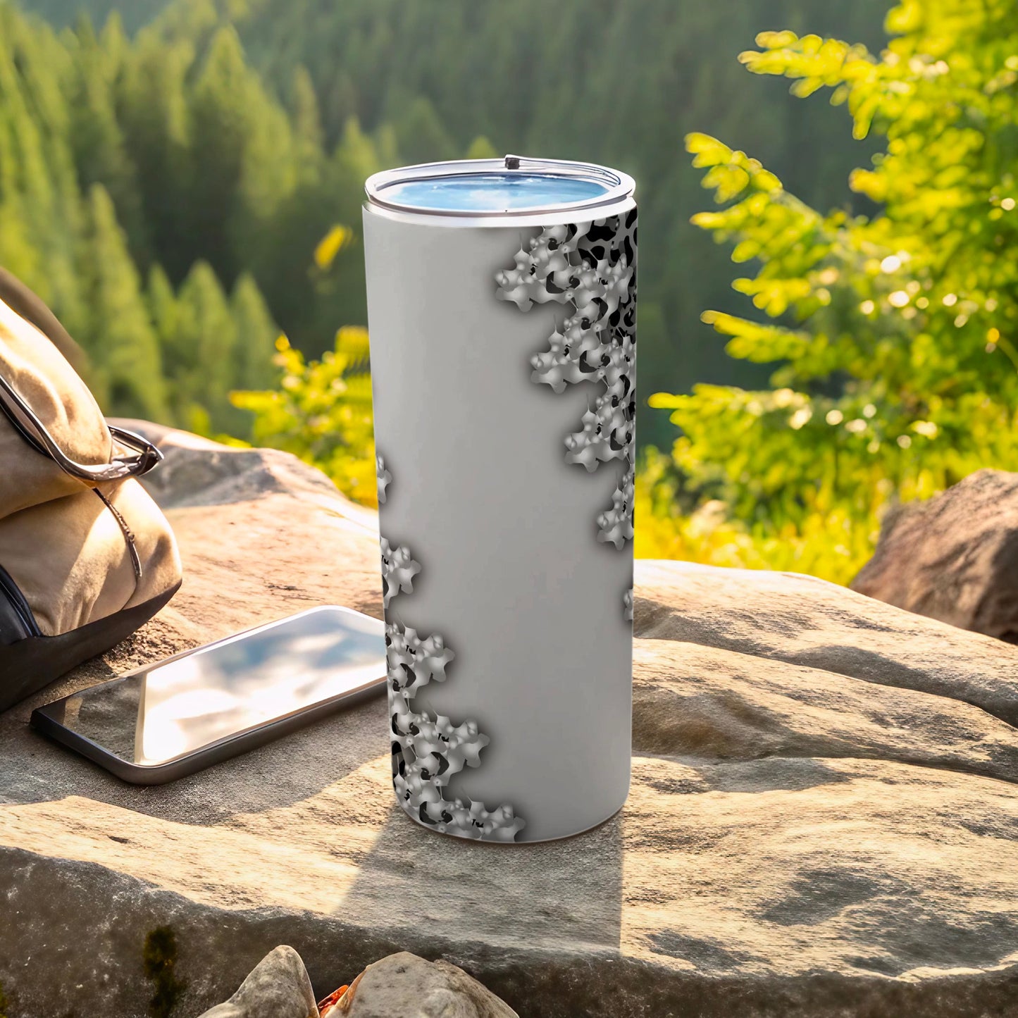 Gray tumbler with a repeating starburst pattern, set outdoors with a backpack and phone.